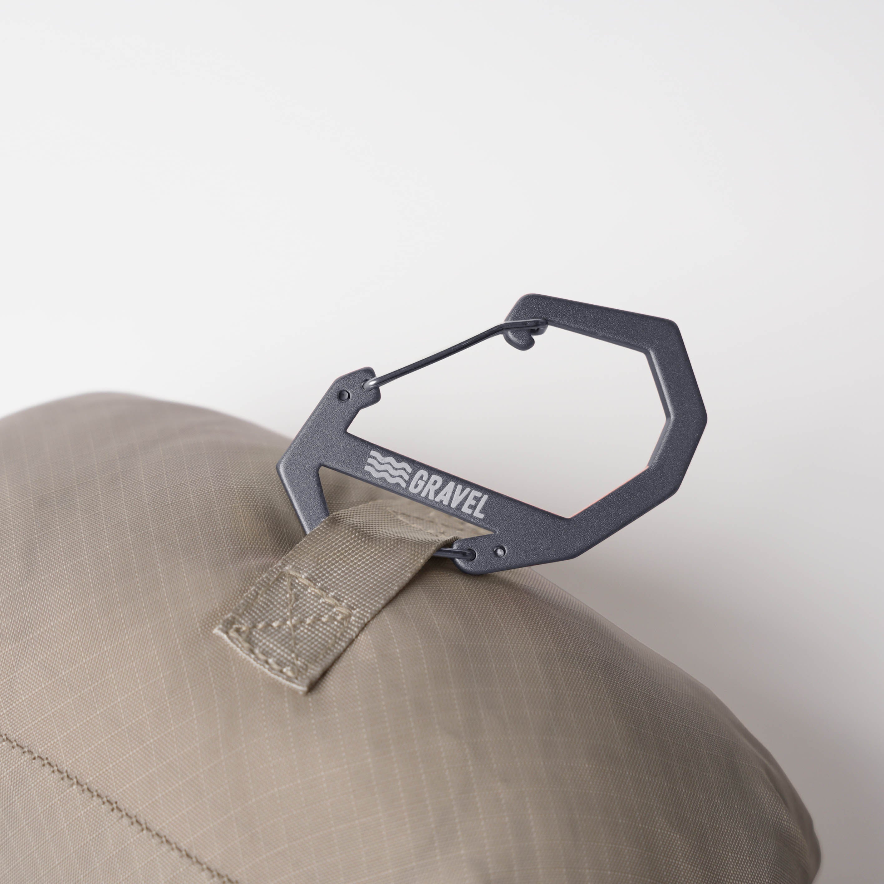 Black carabiner attached to a beige cap with 'Bravel' branding on a light gray background