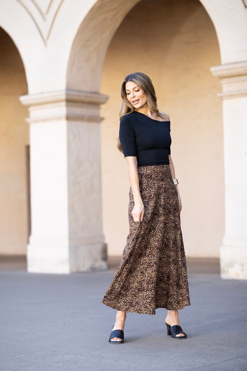 Woman in a black top and patterned skirt standing in front of arched columns.