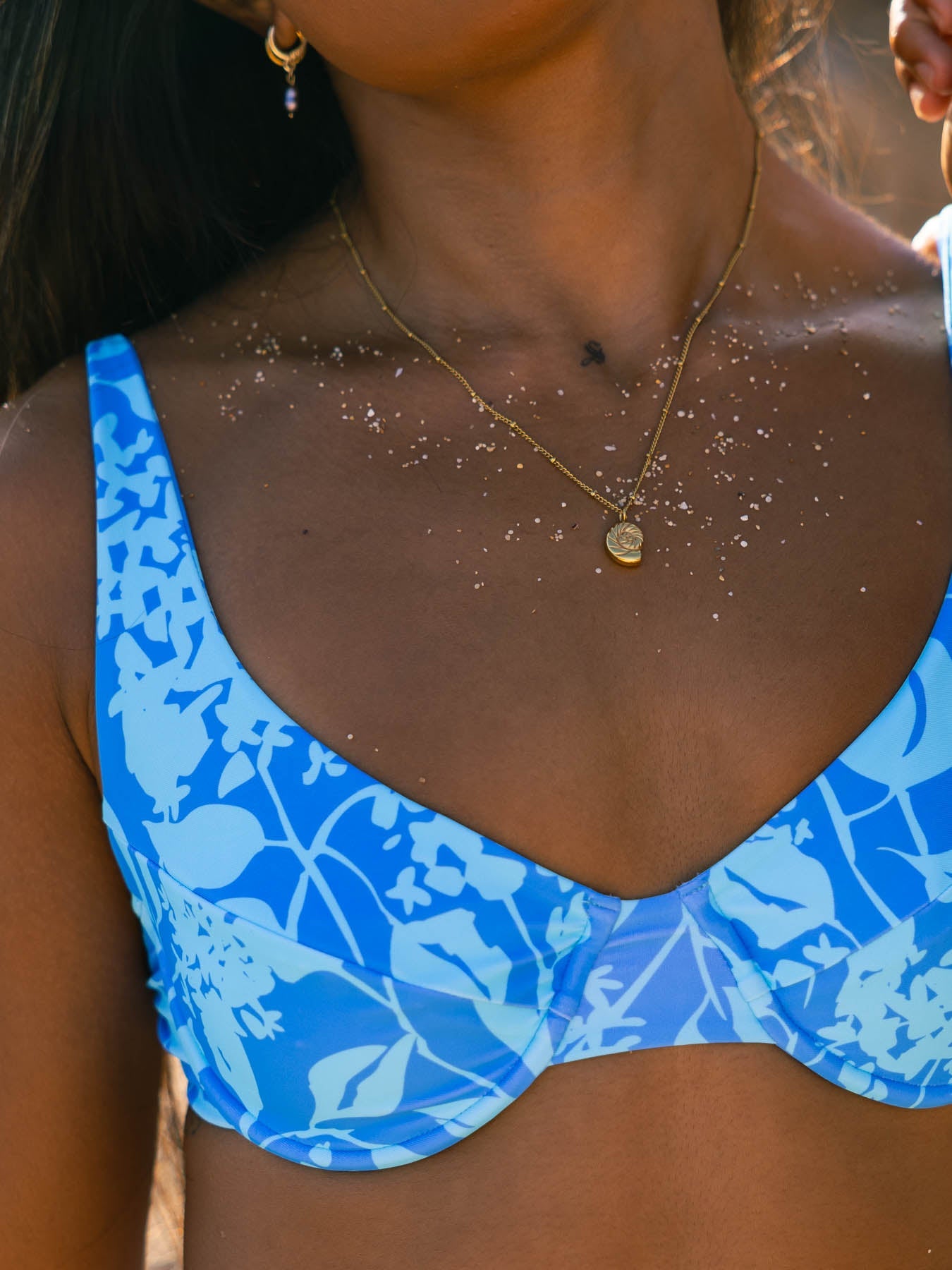 Blue bikini top with floral pattern worn by a person, with a blurred background