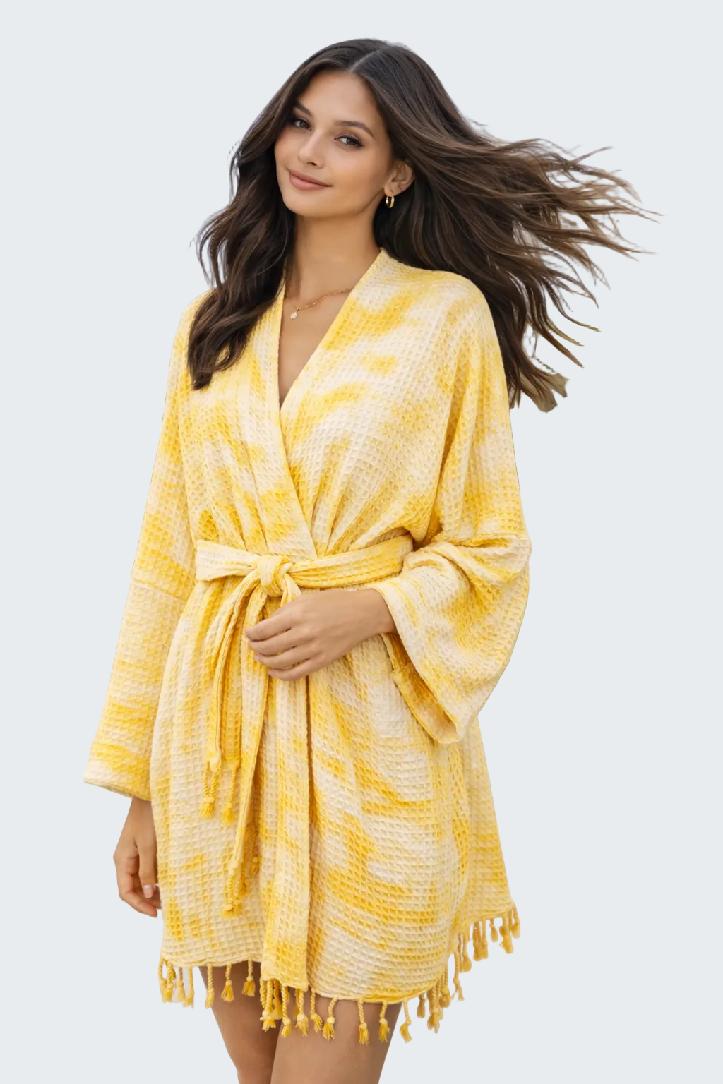 Woman wearing a yellow and white patterned robe on a beach.