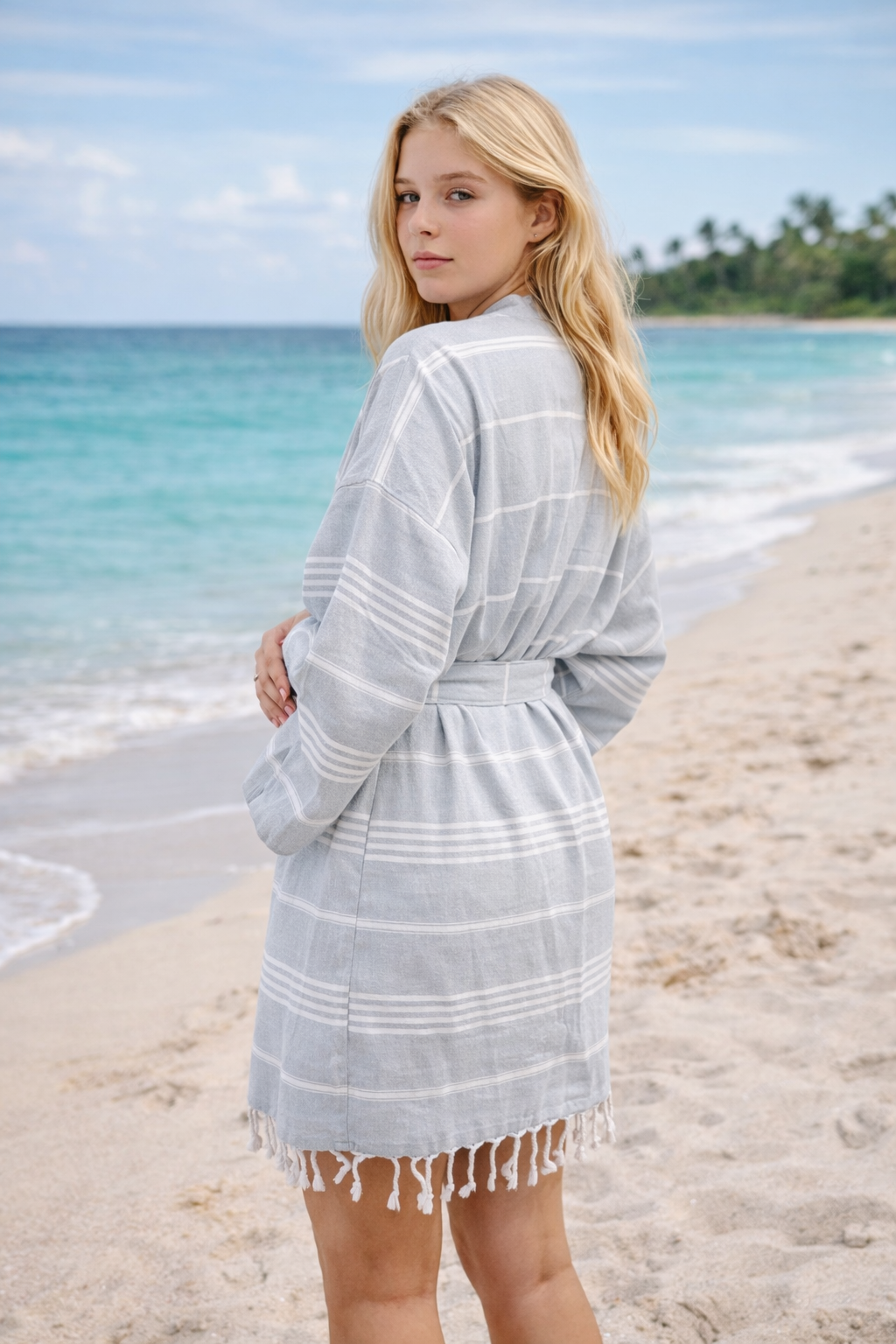 Woman wearing a light gray cover-up with fringe on a beach