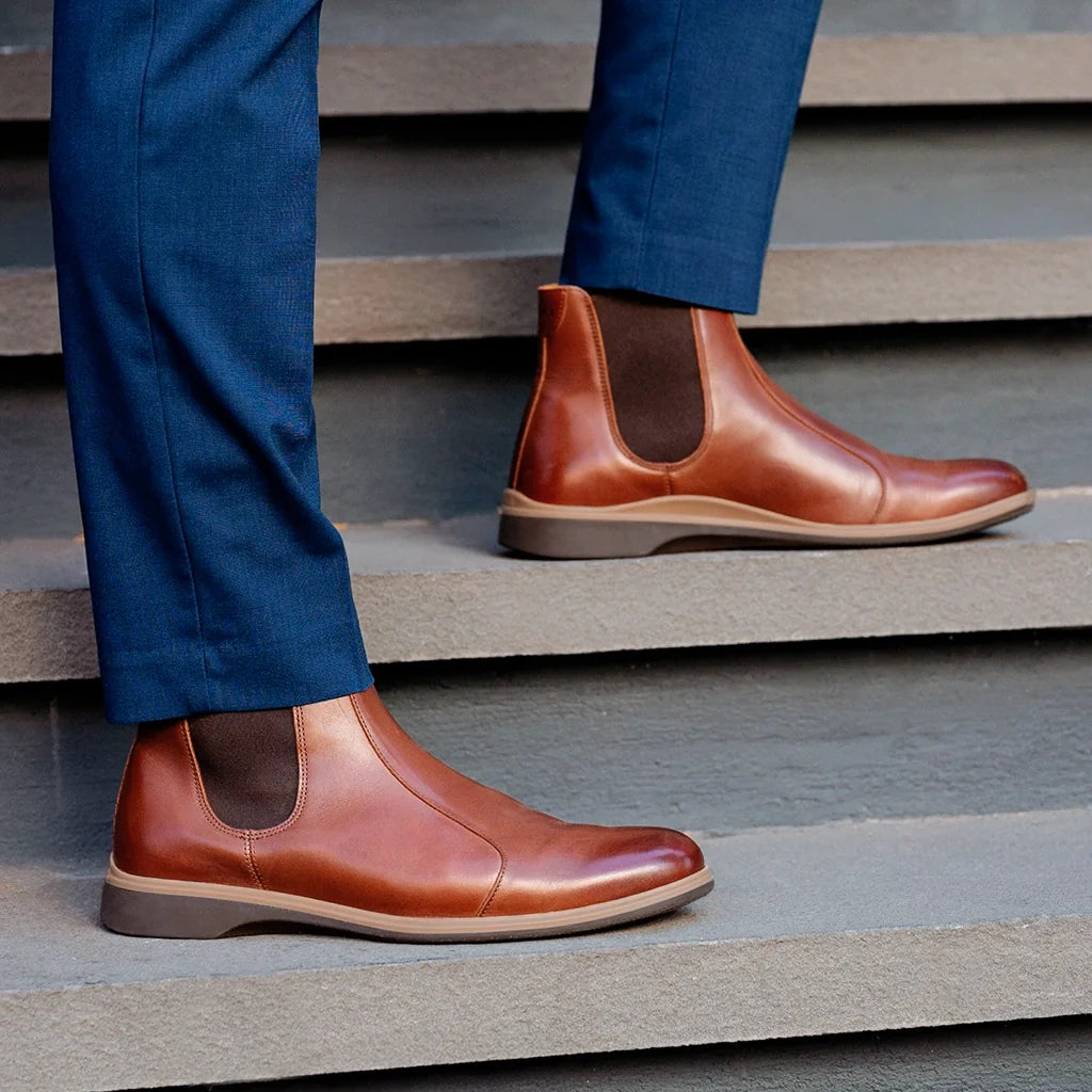 Brown leather Chelsea boots worn with blue pants on a staircase.