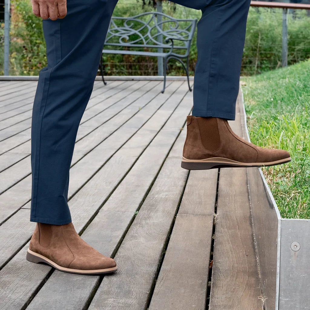 Person wearing brown suede boots and blue pants on a wooden deck.