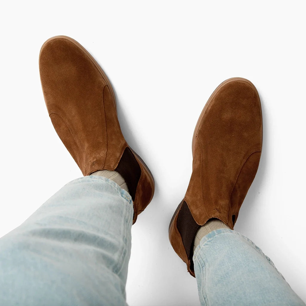 Brown suede shoes worn with light blue jeans on a white background