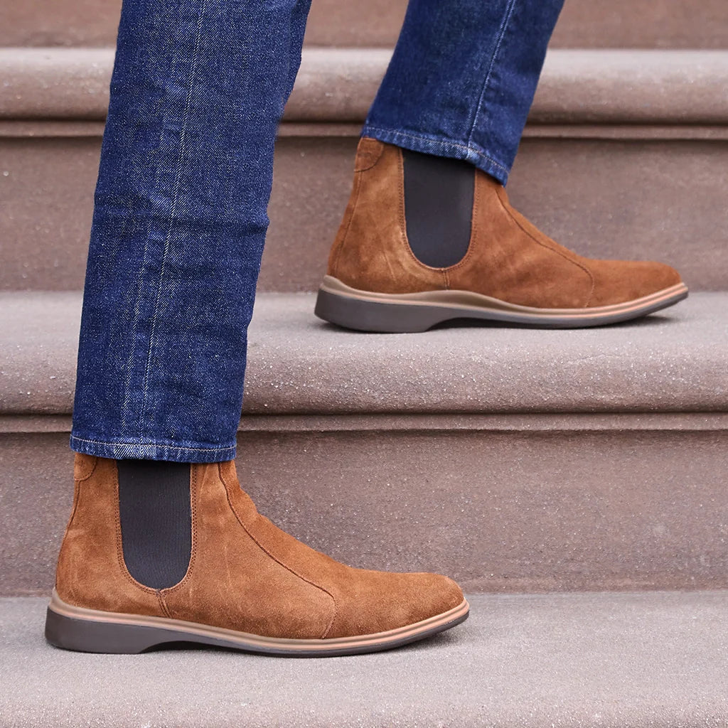 Brown suede Chelsea boots worn with blue jeans on a staircase.