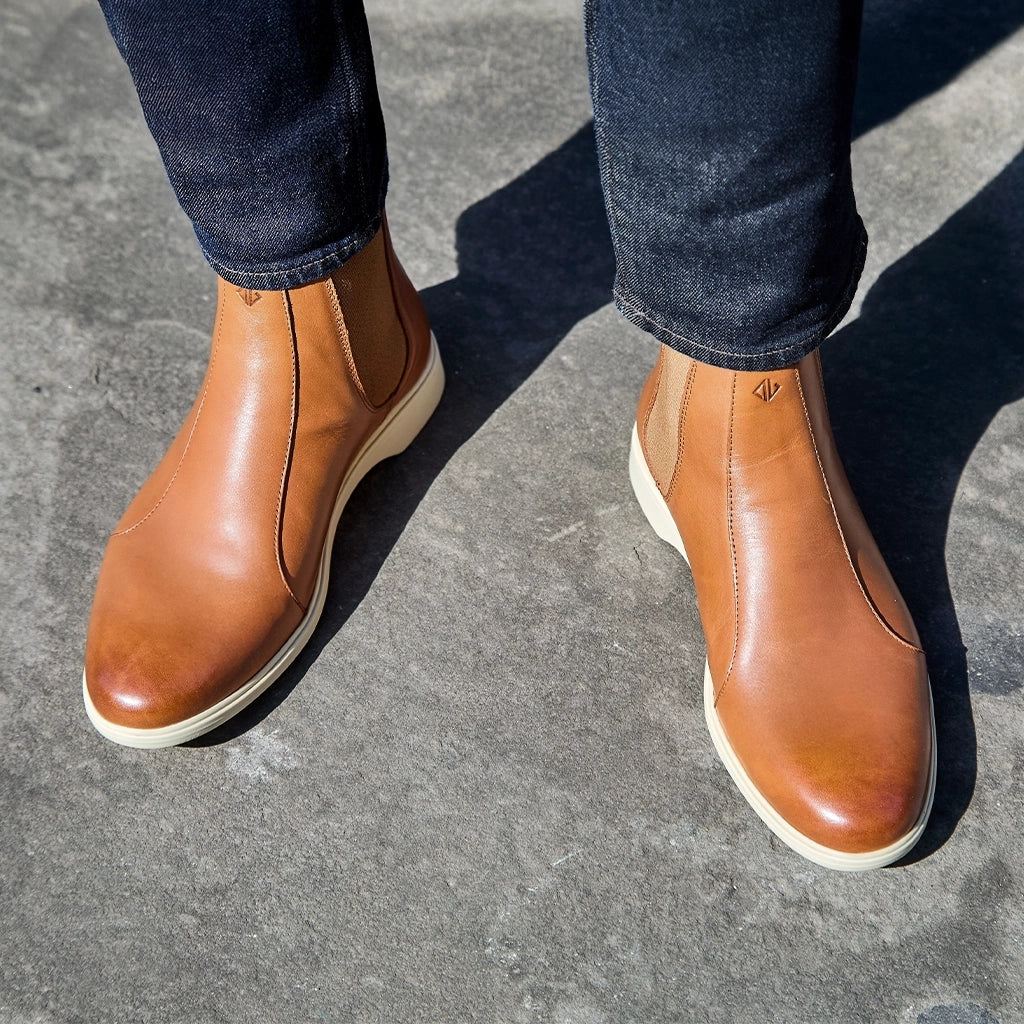 Brown leather shoes worn with dark jeans on a concrete surface