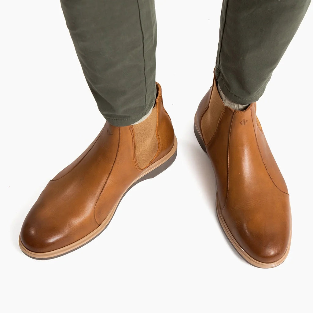Brown leather boots worn with green pants on a white background
