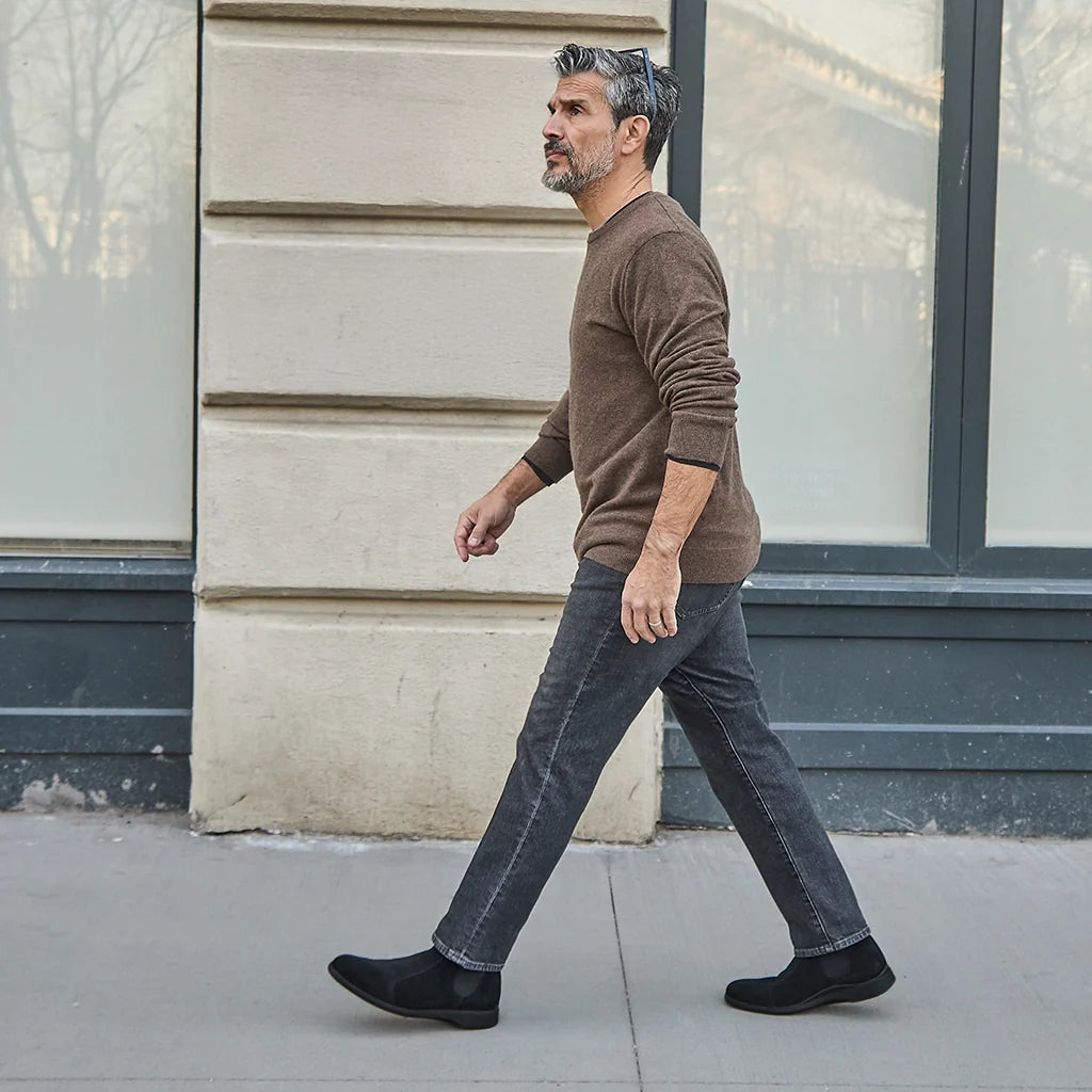 Man walking on a sidewalk wearing a brown sweater and jeans.