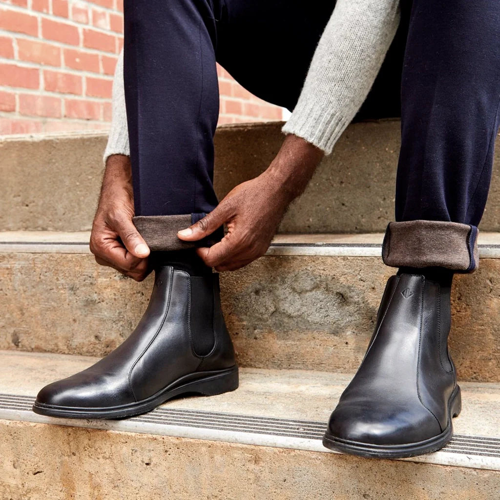 Person wearing black leather boots sitting on steps with a brick wall background