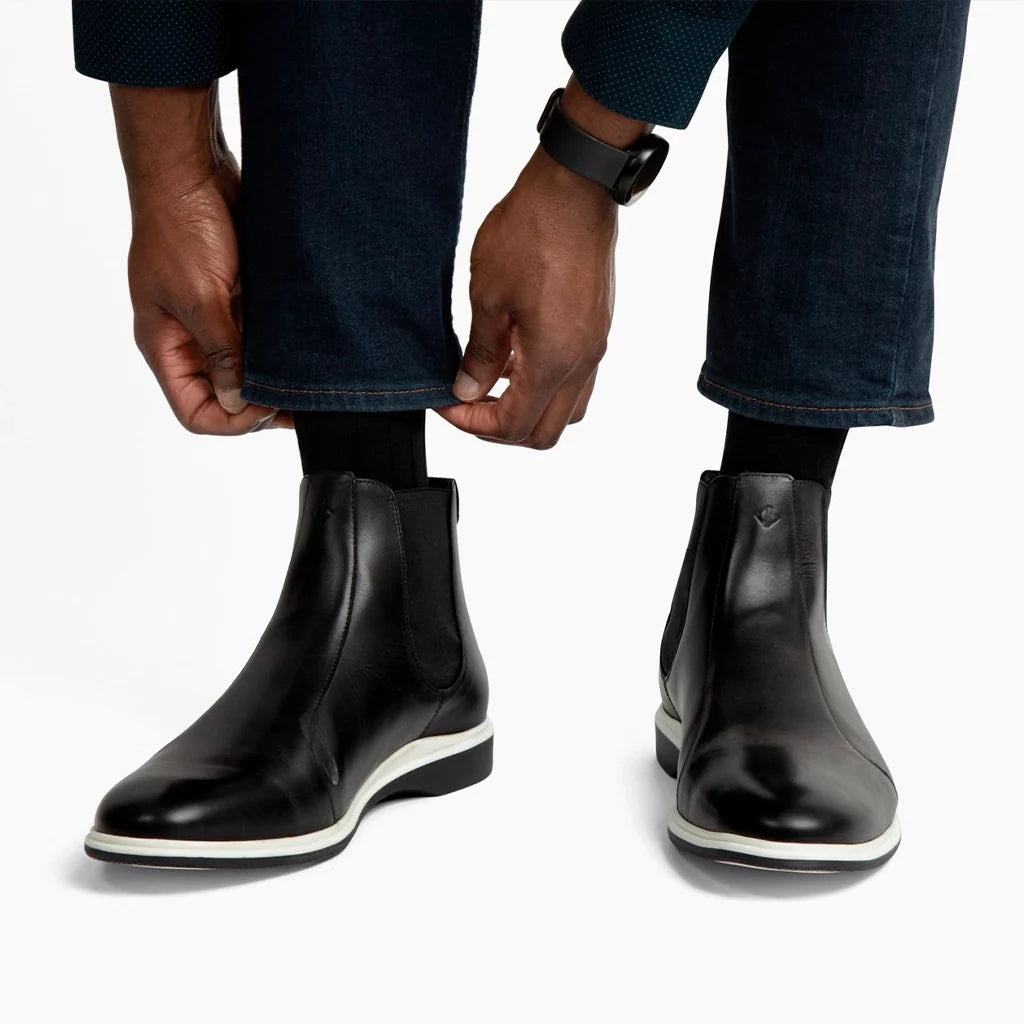 Person wearing black leather boots with white soles on a plain background