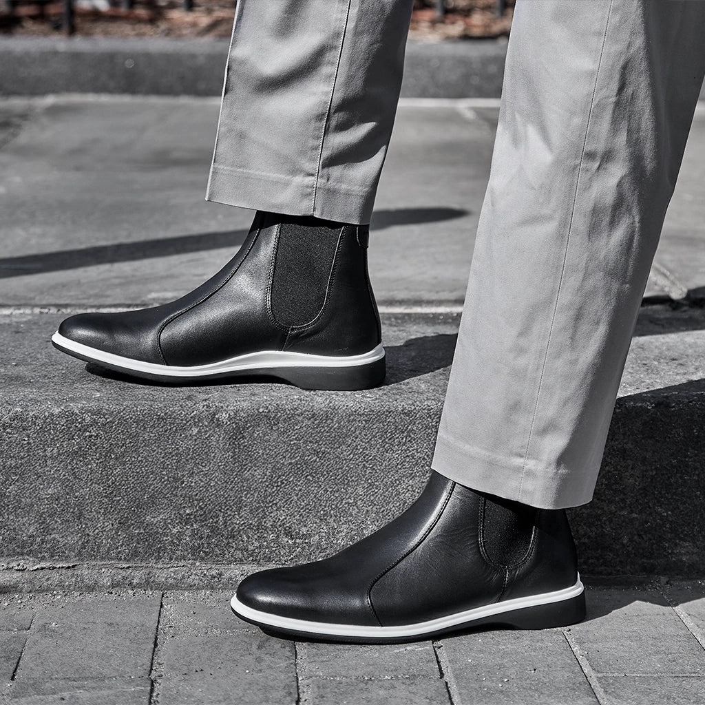 Person wearing black Chelsea boots and light gray pants on a sidewalk.