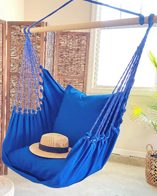 Blue hammock chair with a straw hat on a wooden stand in a bright room.
