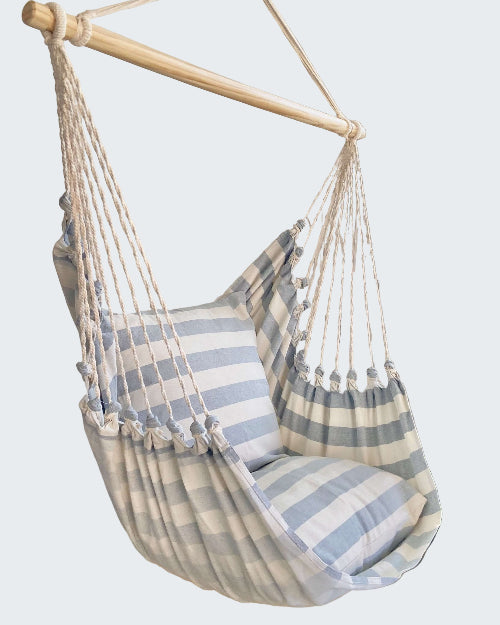Striped hammock chair hanging from a wooden rod with a decorative white screen in the background.
