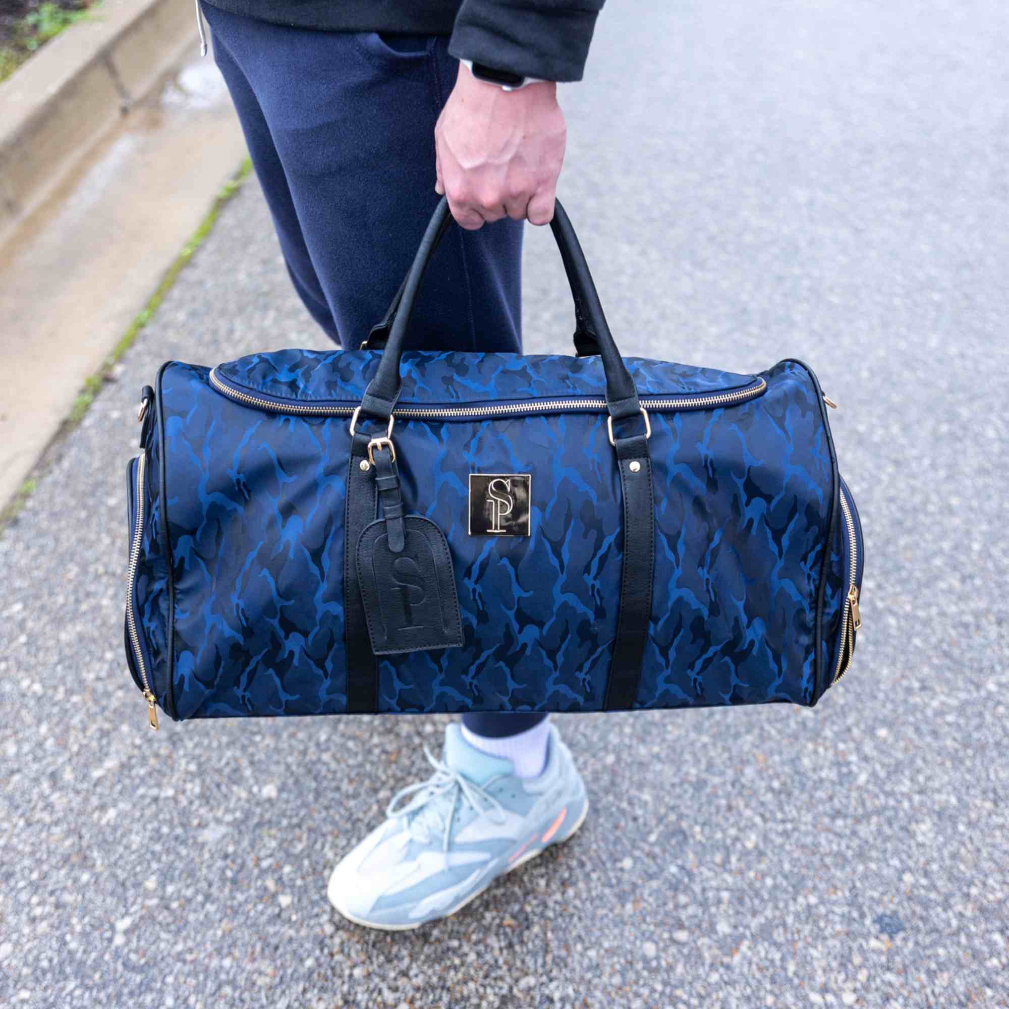Person holding a blue patterned duffel bag on a street