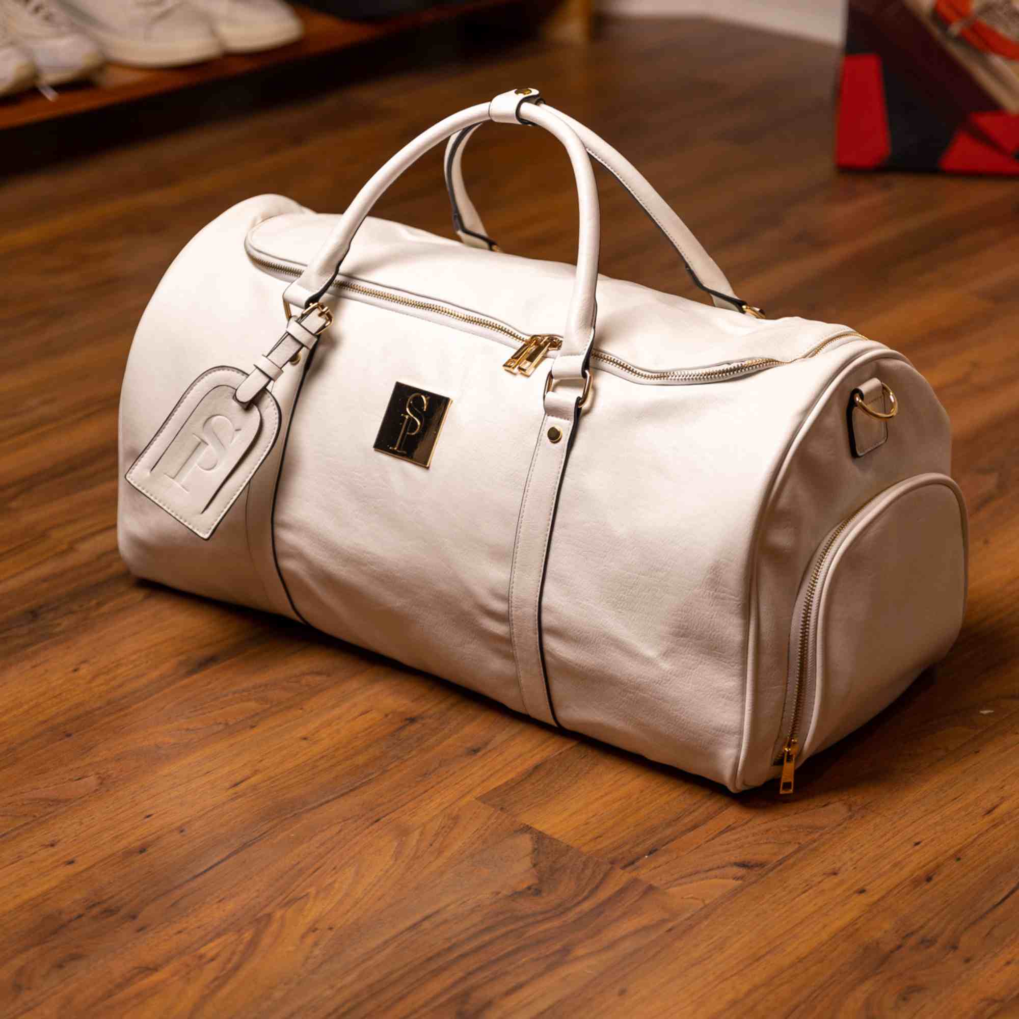 White duffel bag with gold accents on a wooden floor