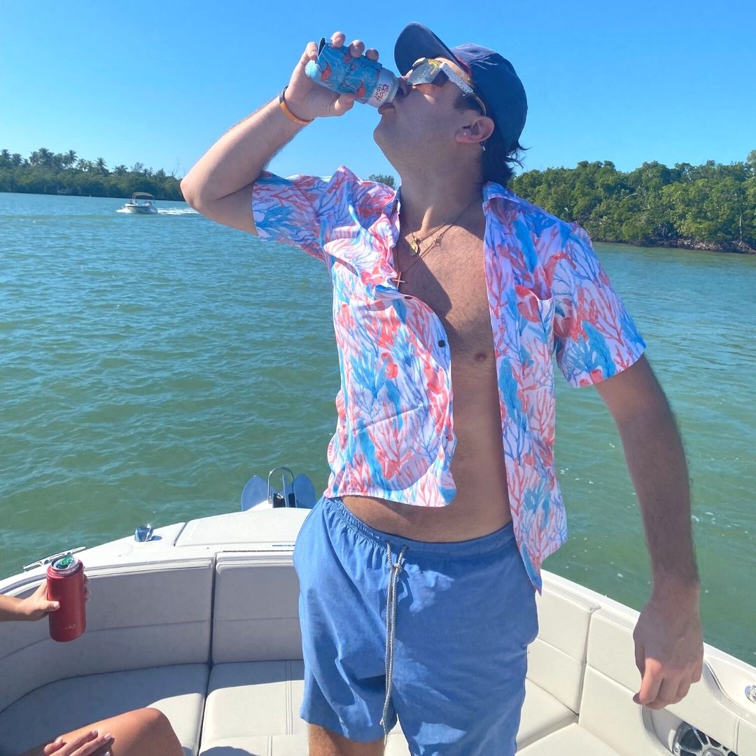 Man in colorful shirt and blue shorts drinking from a can on a boat