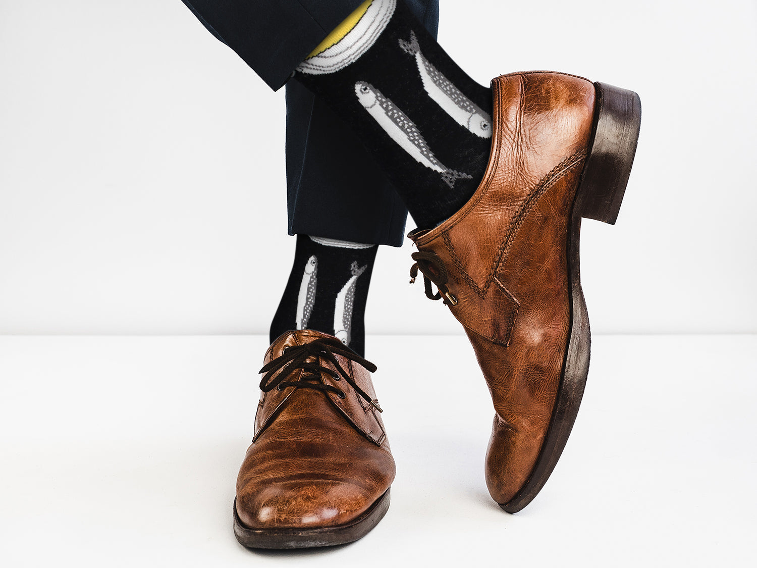 Brown leather shoes worn with black pants and socks on a white background