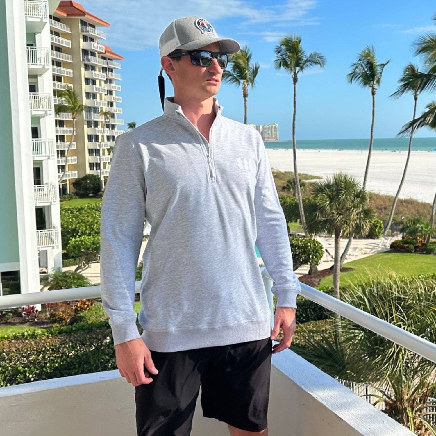Man standing on a balcony with a beach and palm trees in the background