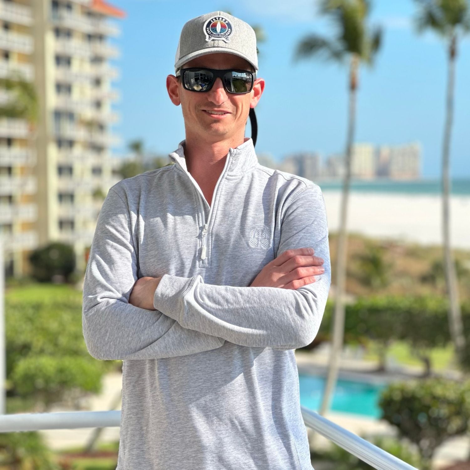 Man wearing sunglasses and a cap with a cityscape and pool in the background