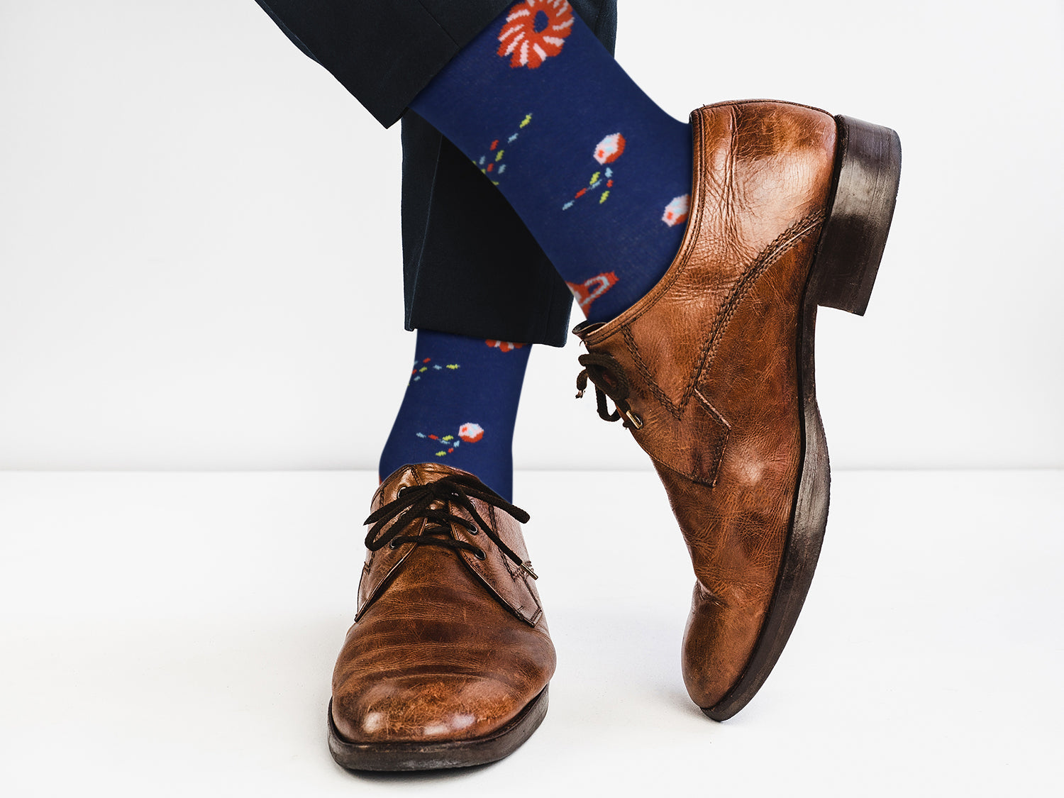 Brown leather shoes with blue socks featuring colorful designs on a white background