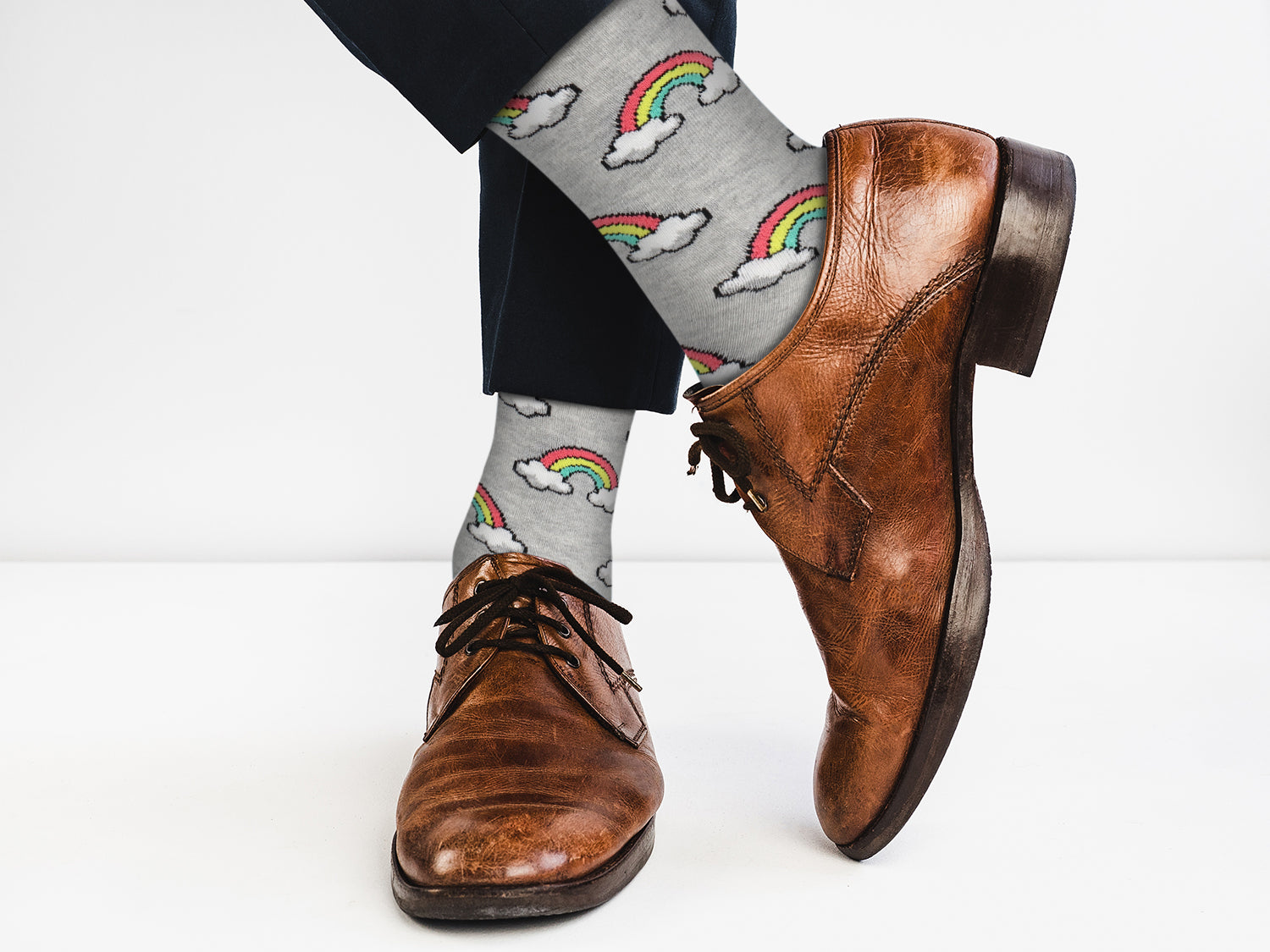 Brown dress shoes with gray socks featuring rainbow and cloud designs on a white background