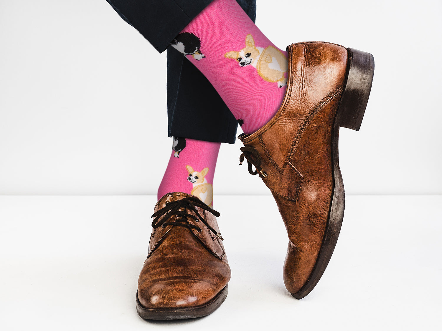 Person wearing pink socks with dog patterns and brown shoes on a white background