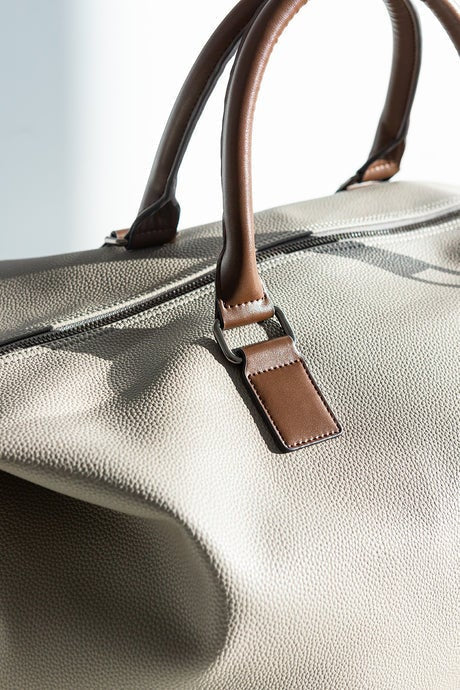 Close-up of a beige leather bag with brown handles and strap.