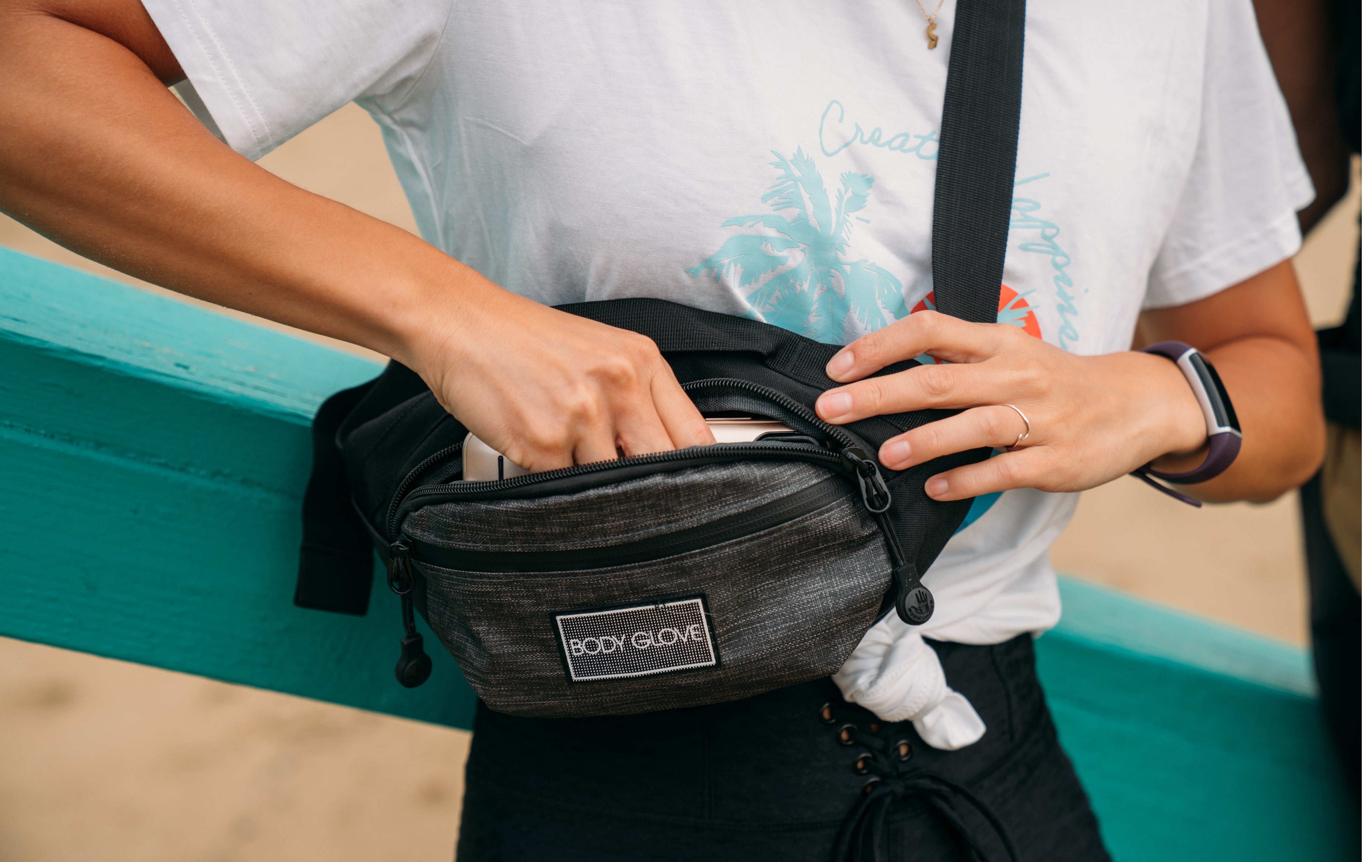 Person wearing a black fanny pack with 'Body Glove' branding on a beach.