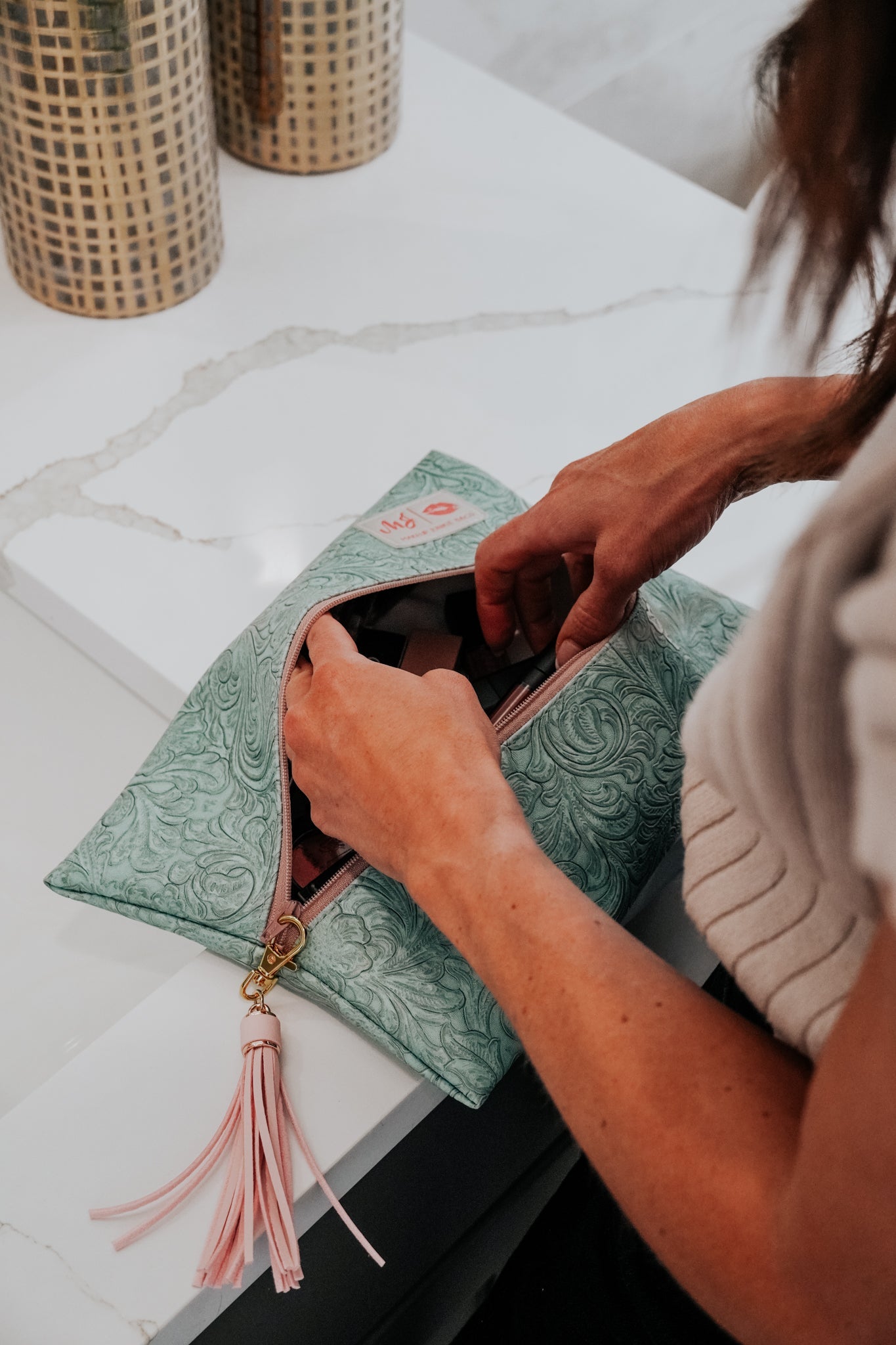 Person opening a green clutch with floral patterns on a white surface