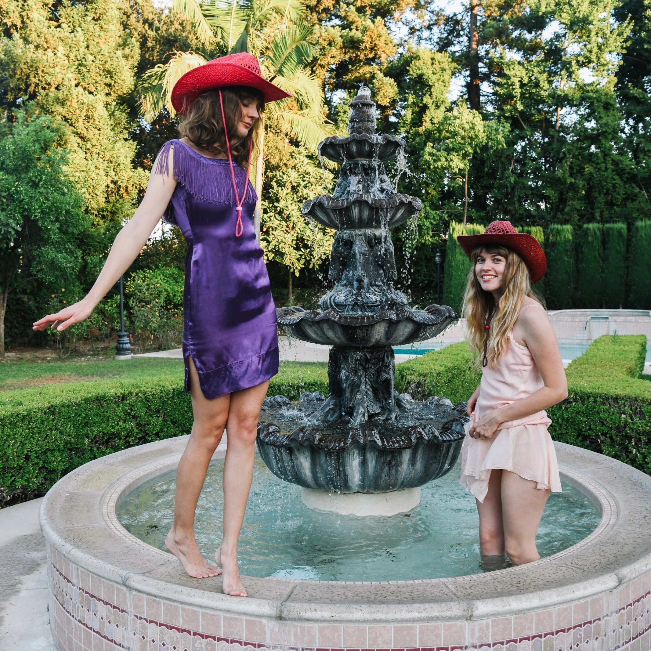Two women in hats standing by a fountain in a garden
