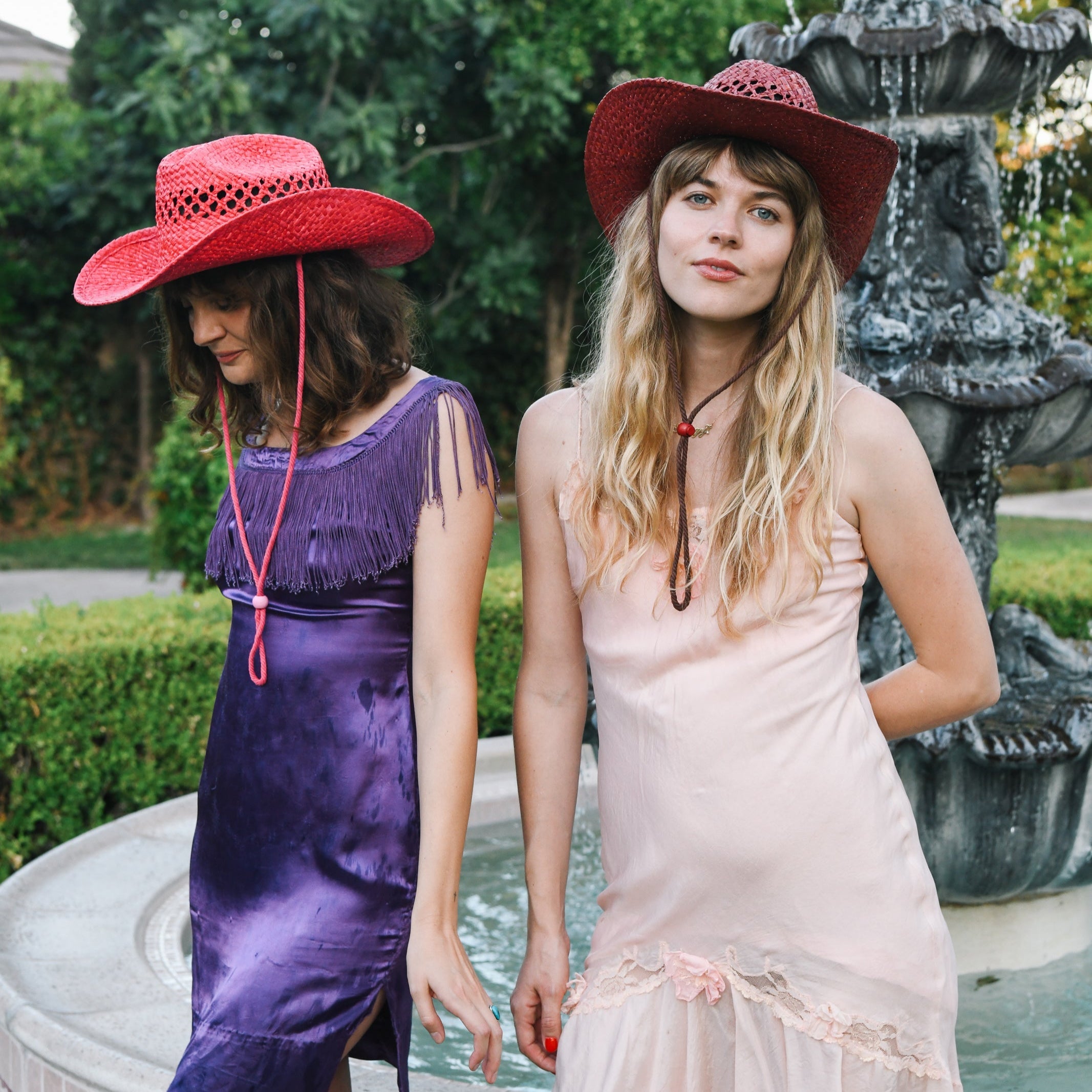 Two women wearing red hats standing in front of a fountain.