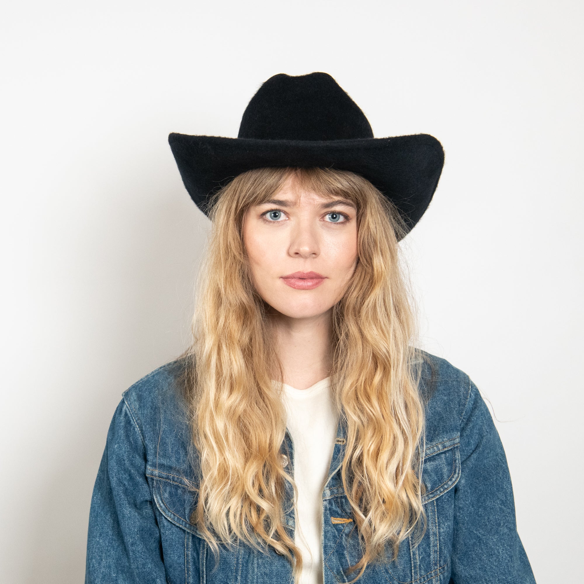 Person wearing a black cowboy hat and denim jacket on a white background