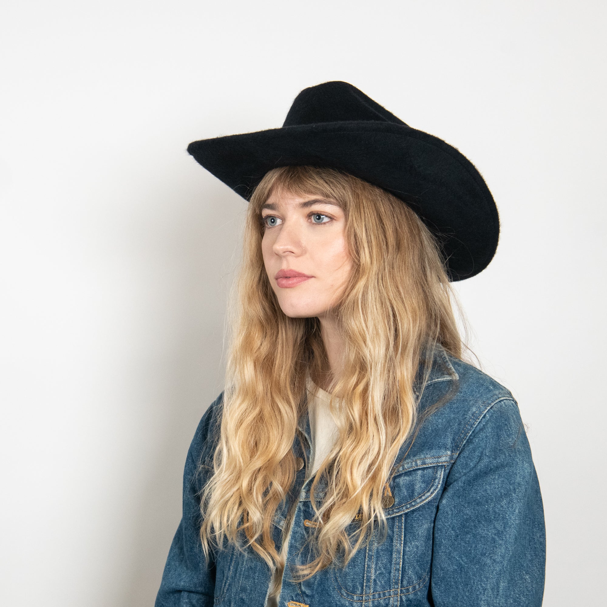 Woman wearing a black hat and denim jacket against a white background