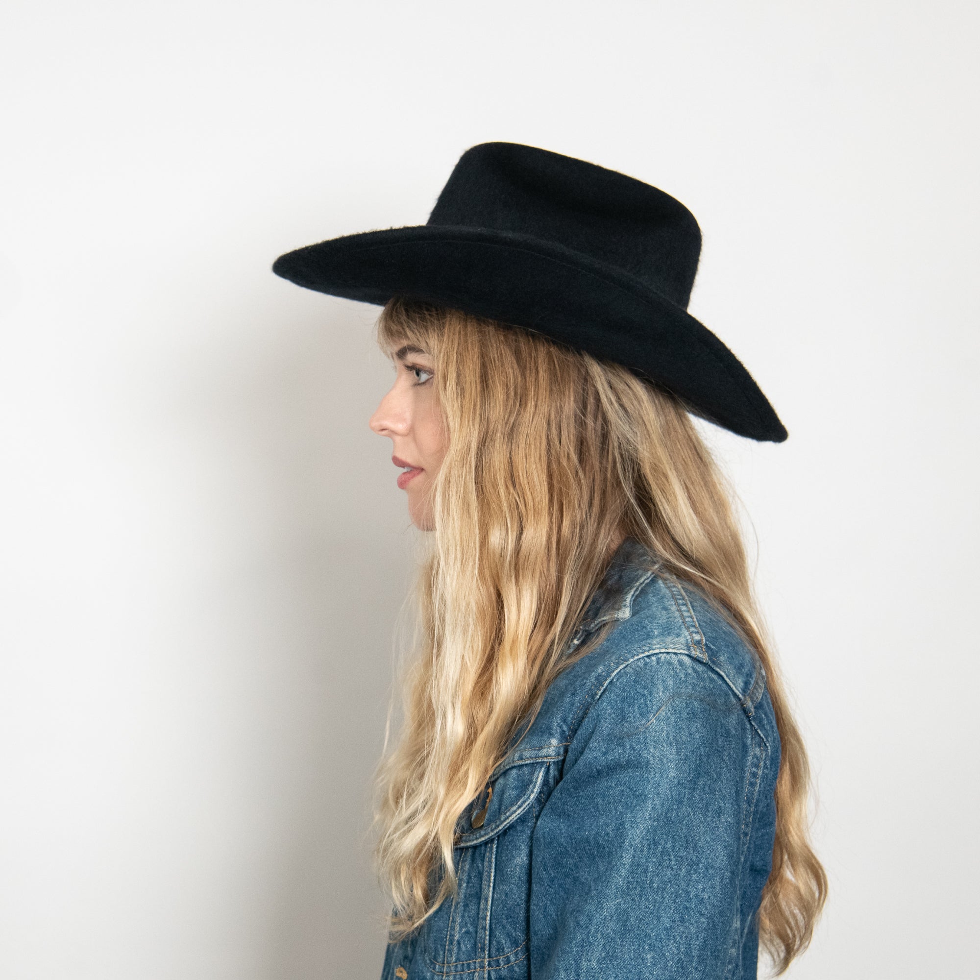 Woman wearing a black hat and denim jacket against a white background