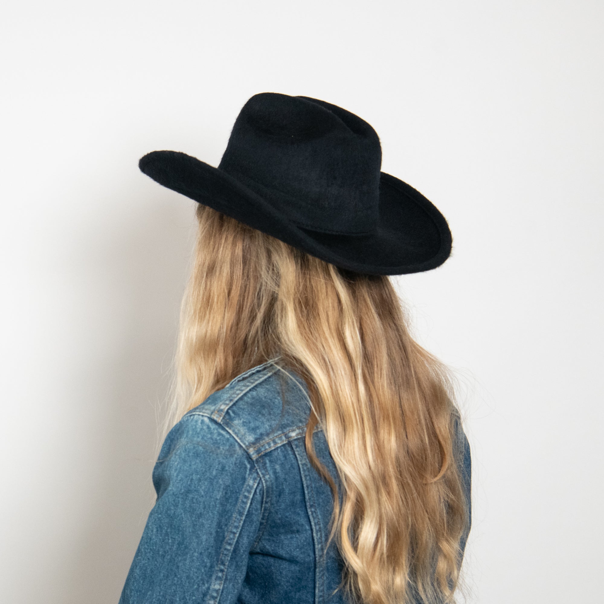 Person wearing a black cowboy hat and denim jacket against a white background