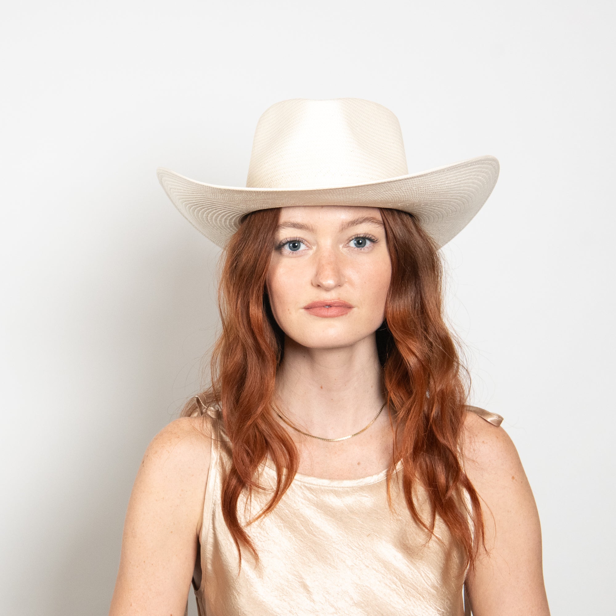 Woman wearing a white cowboy hat against a plain background