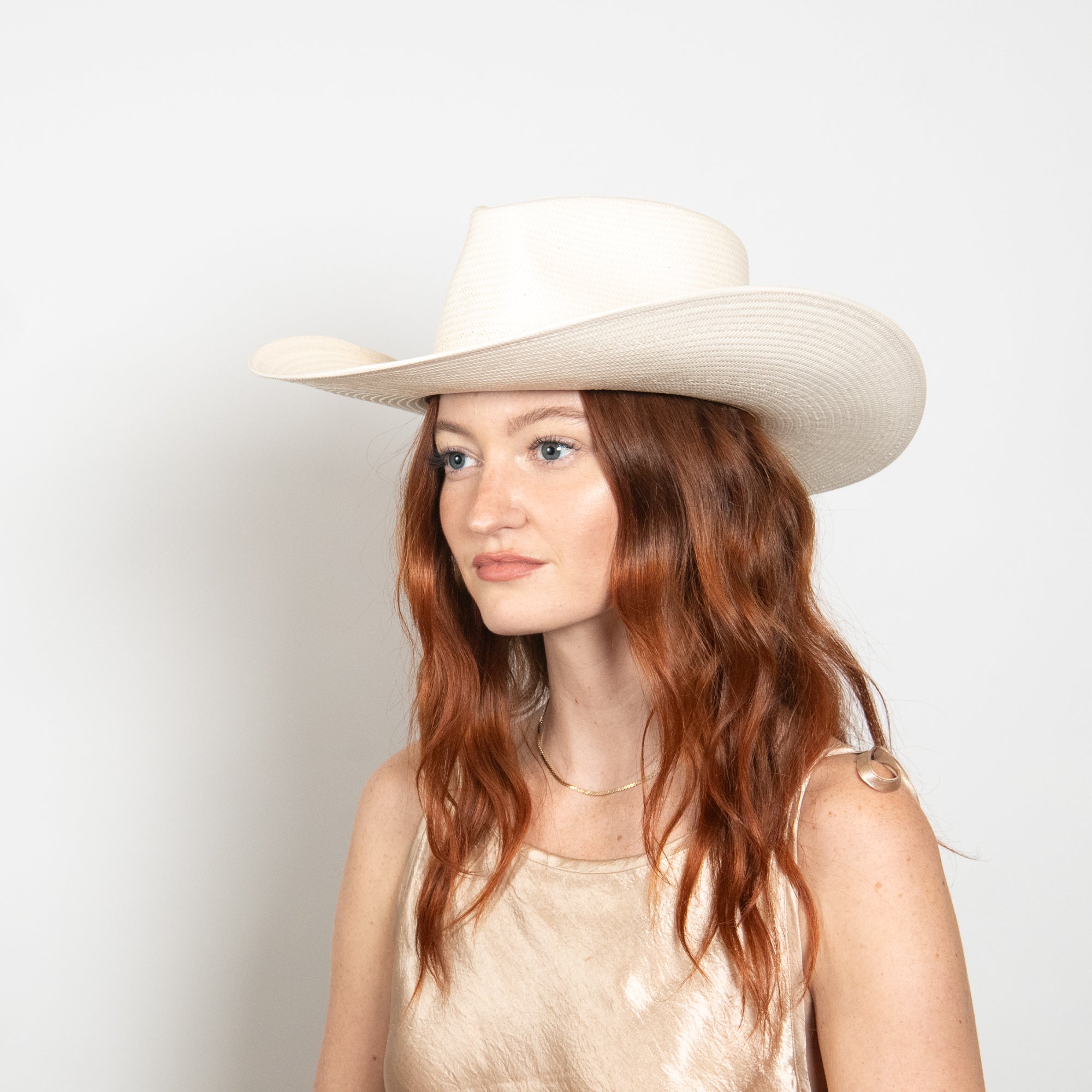 Woman wearing a wide-brimmed beige hat against a plain background