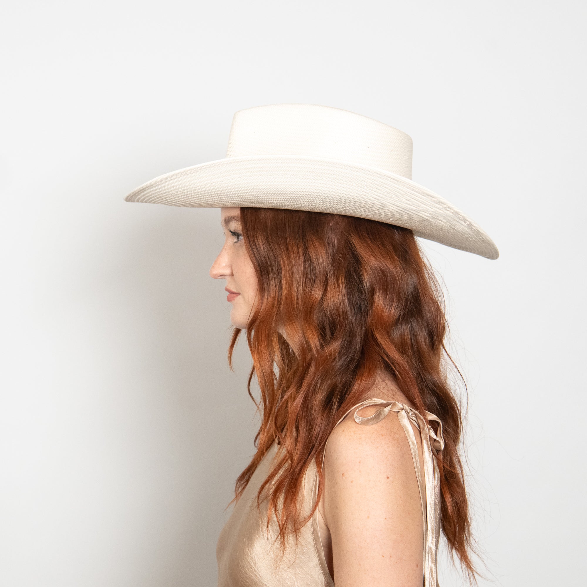Woman wearing a white wide-brimmed hat against a light background