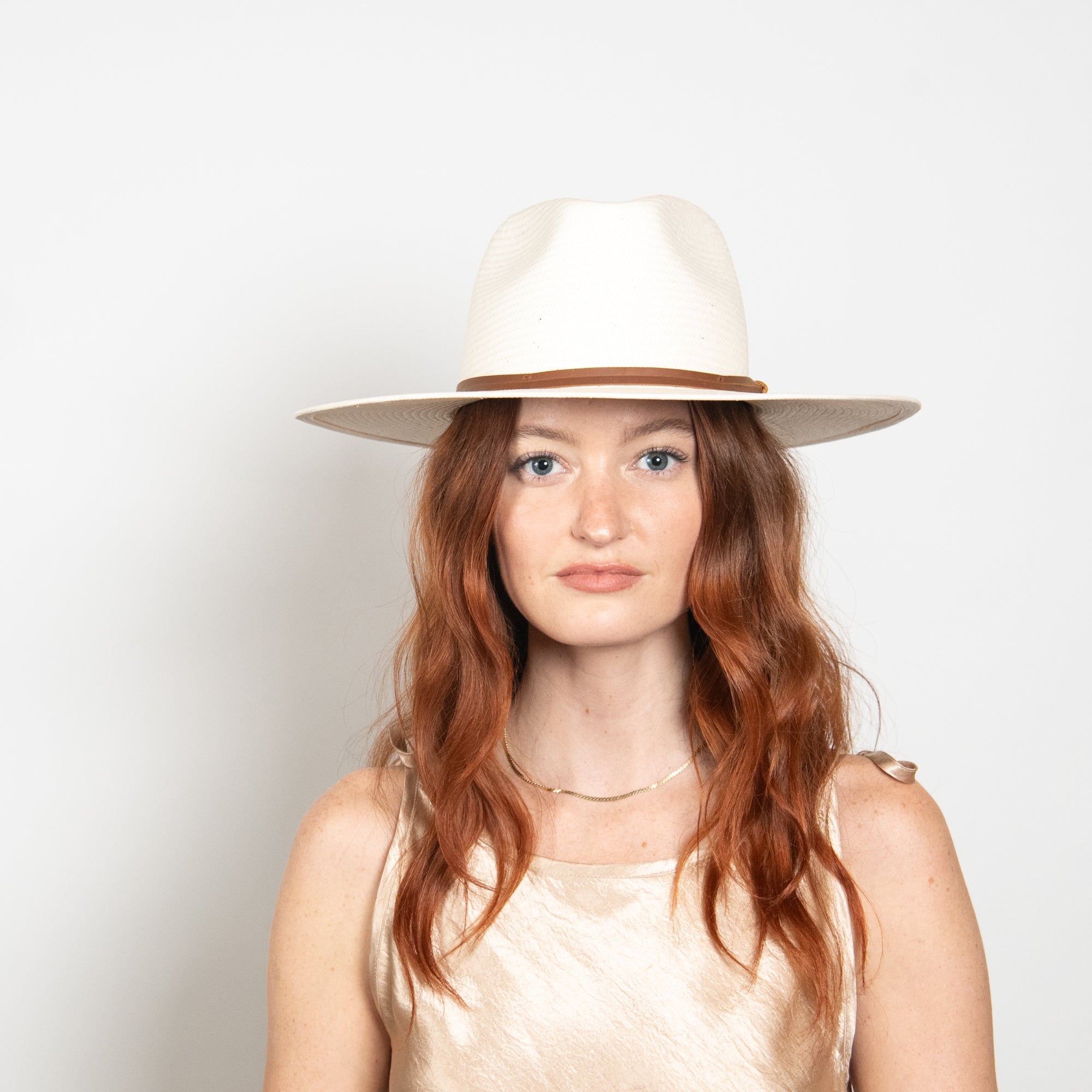 Woman wearing a white hat with a brown band on a plain background