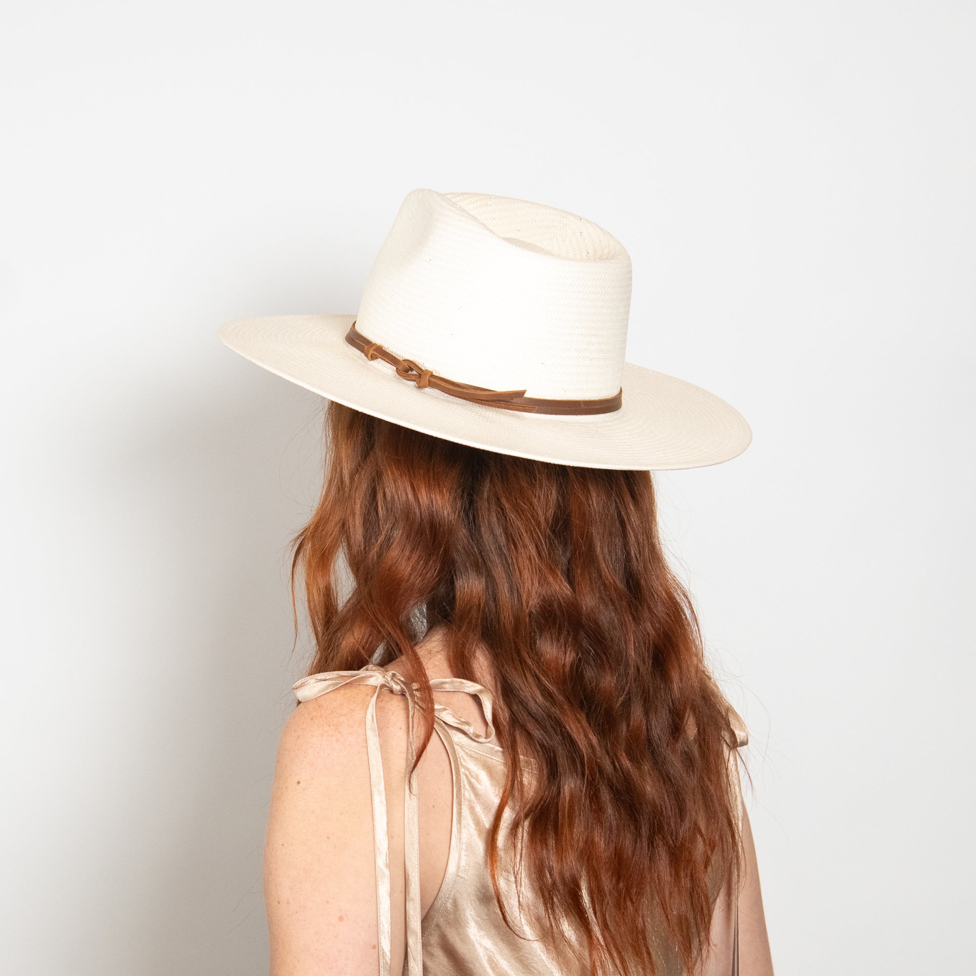 Person wearing a beige hat with a brown band on a plain background