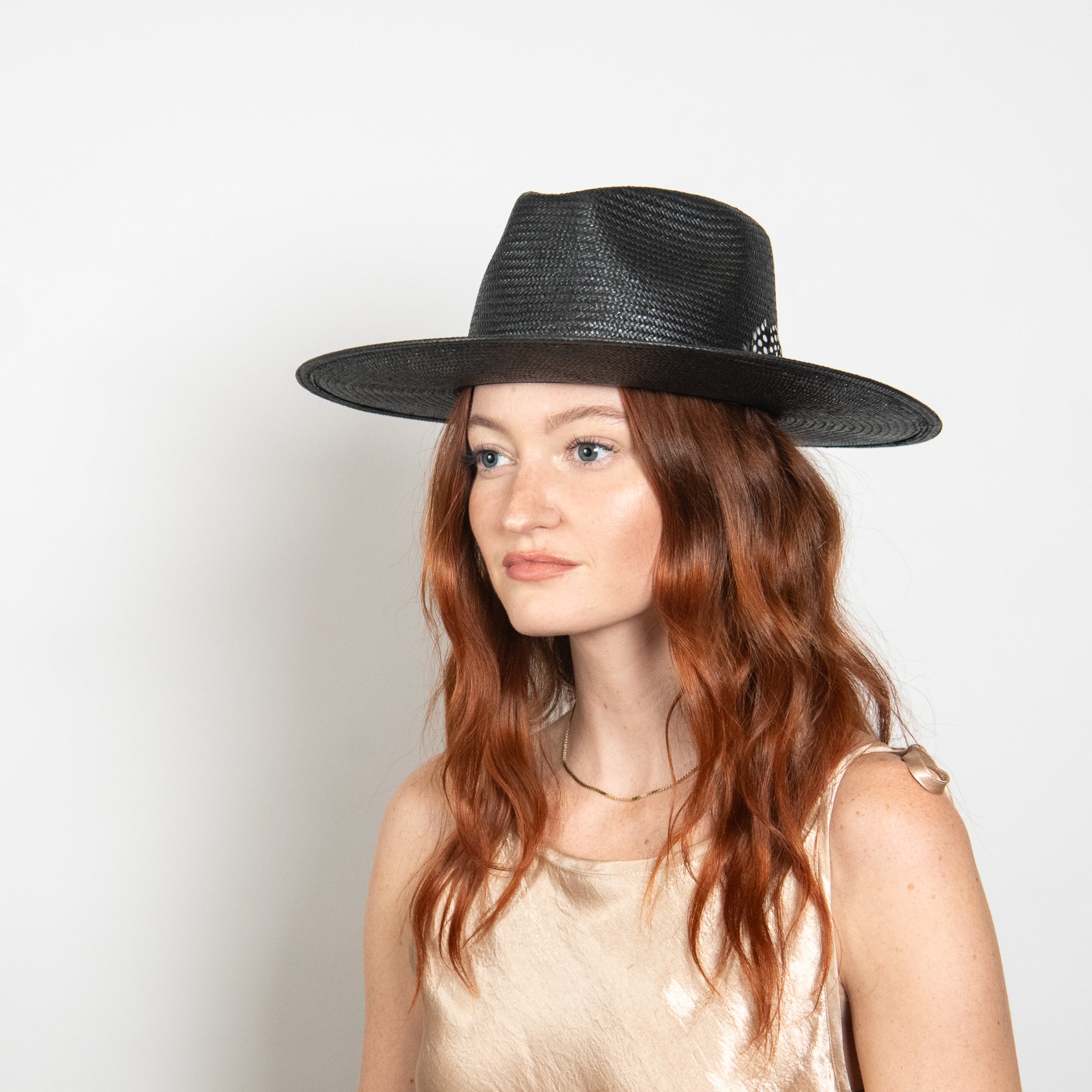 Woman wearing a black fedora hat against a plain background