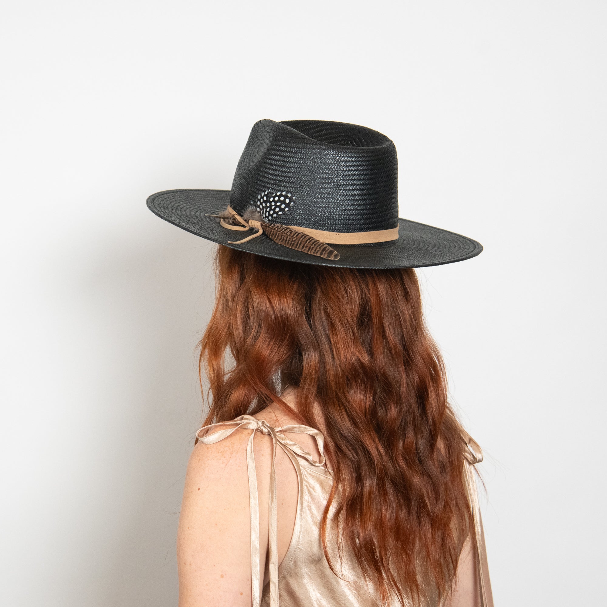 Person wearing a black straw hat with a feather on a plain background