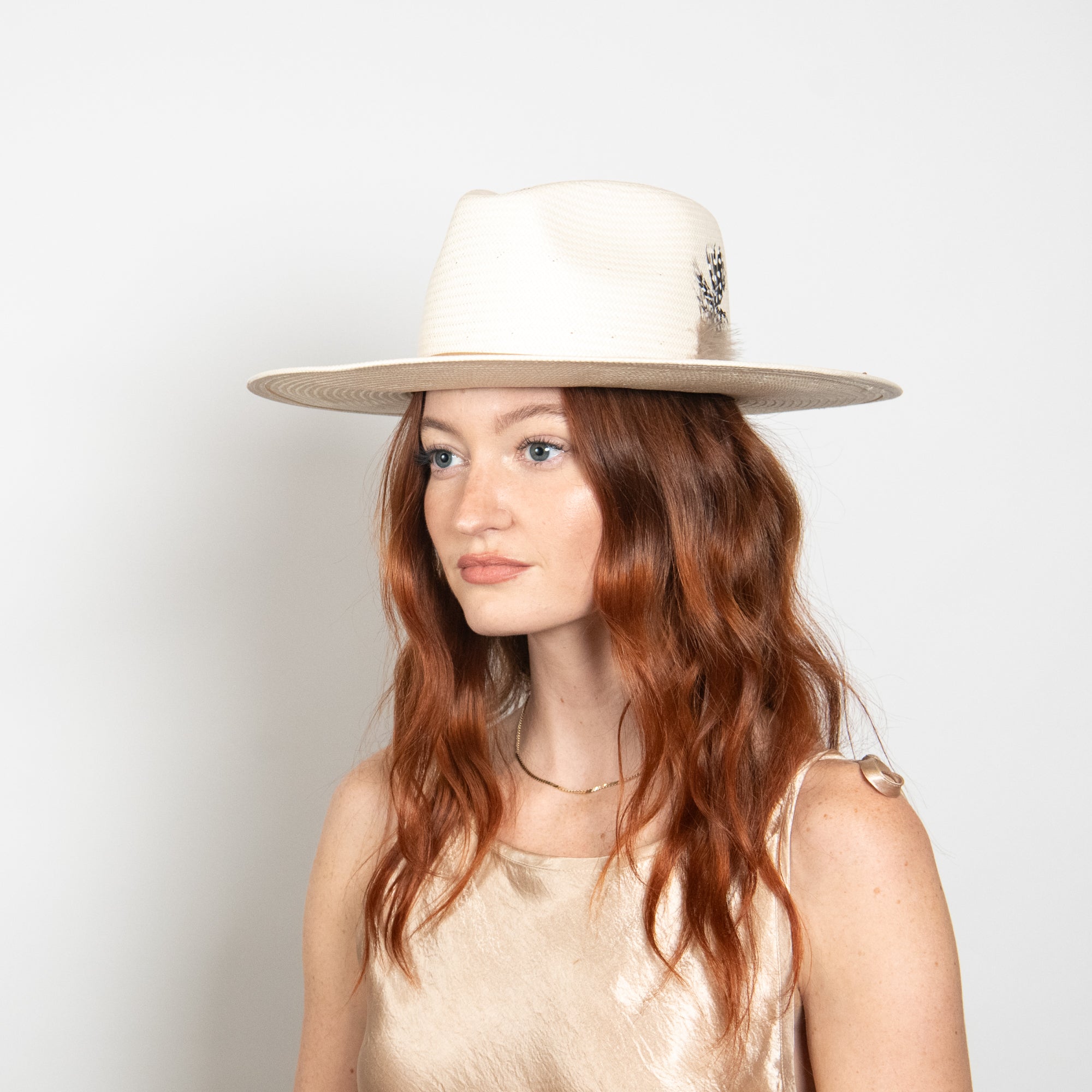Woman wearing a white wide-brimmed hat against a plain background