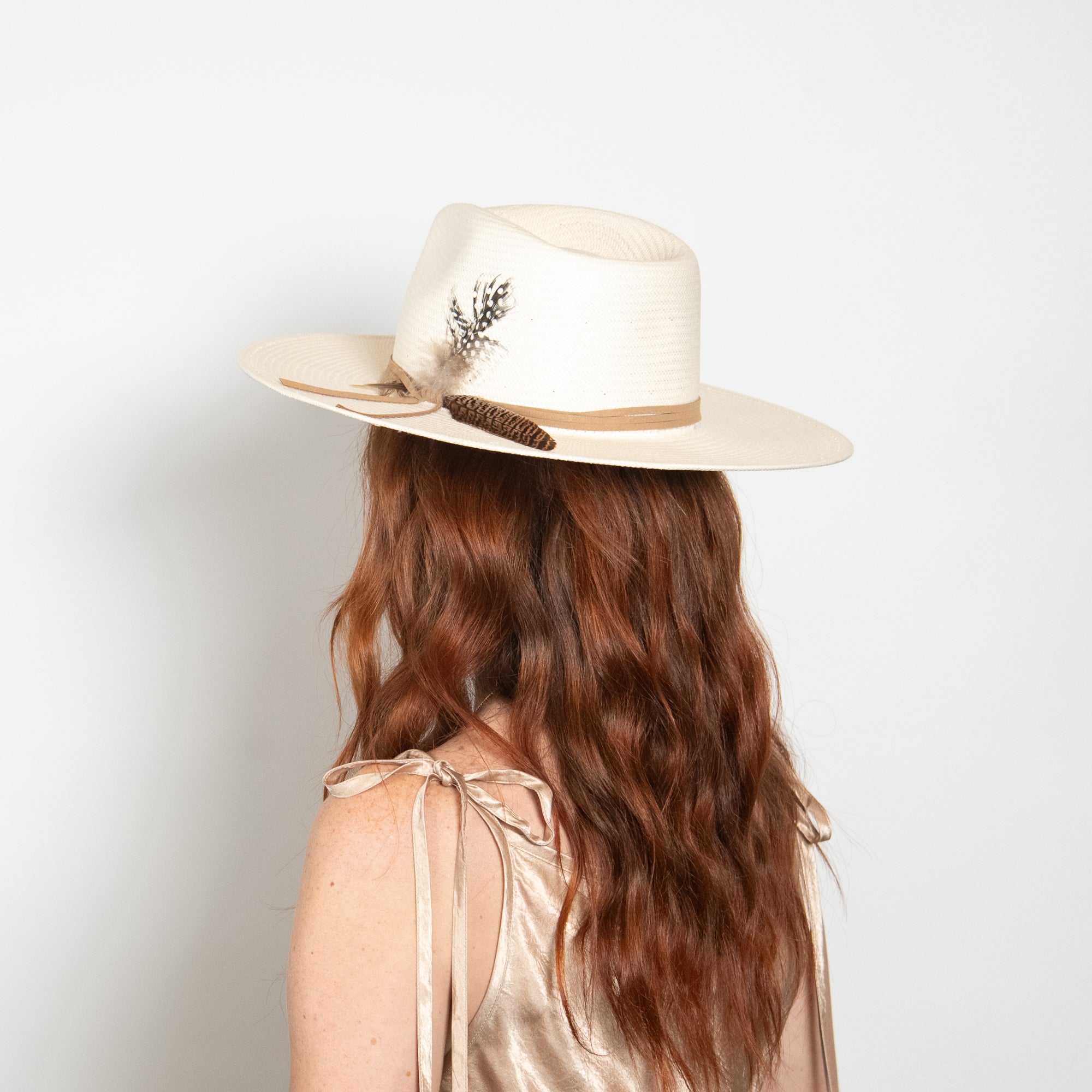 Person wearing a beige hat with a feather against a light gray background