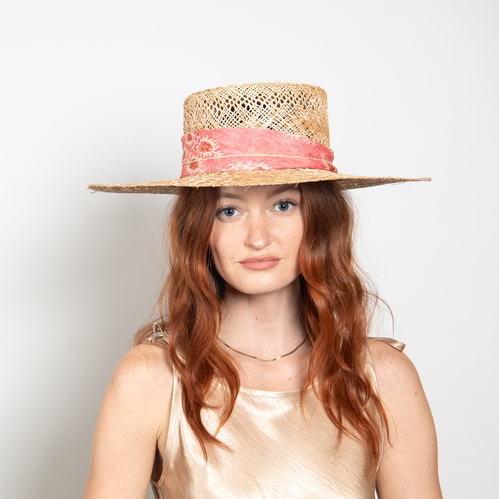 Woman wearing a straw hat with a pink band against a plain background