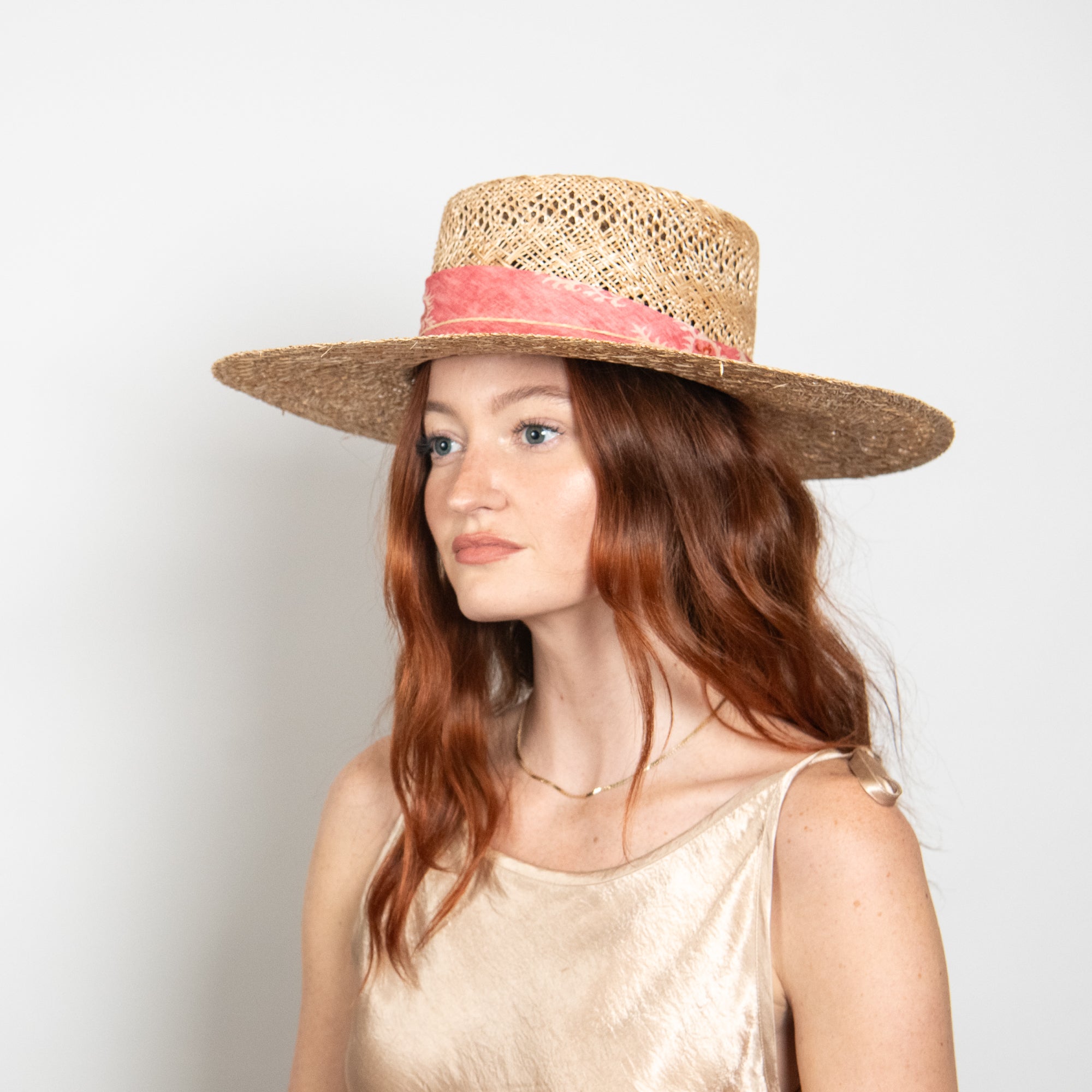 Woman wearing a straw hat with a red band on a plain background