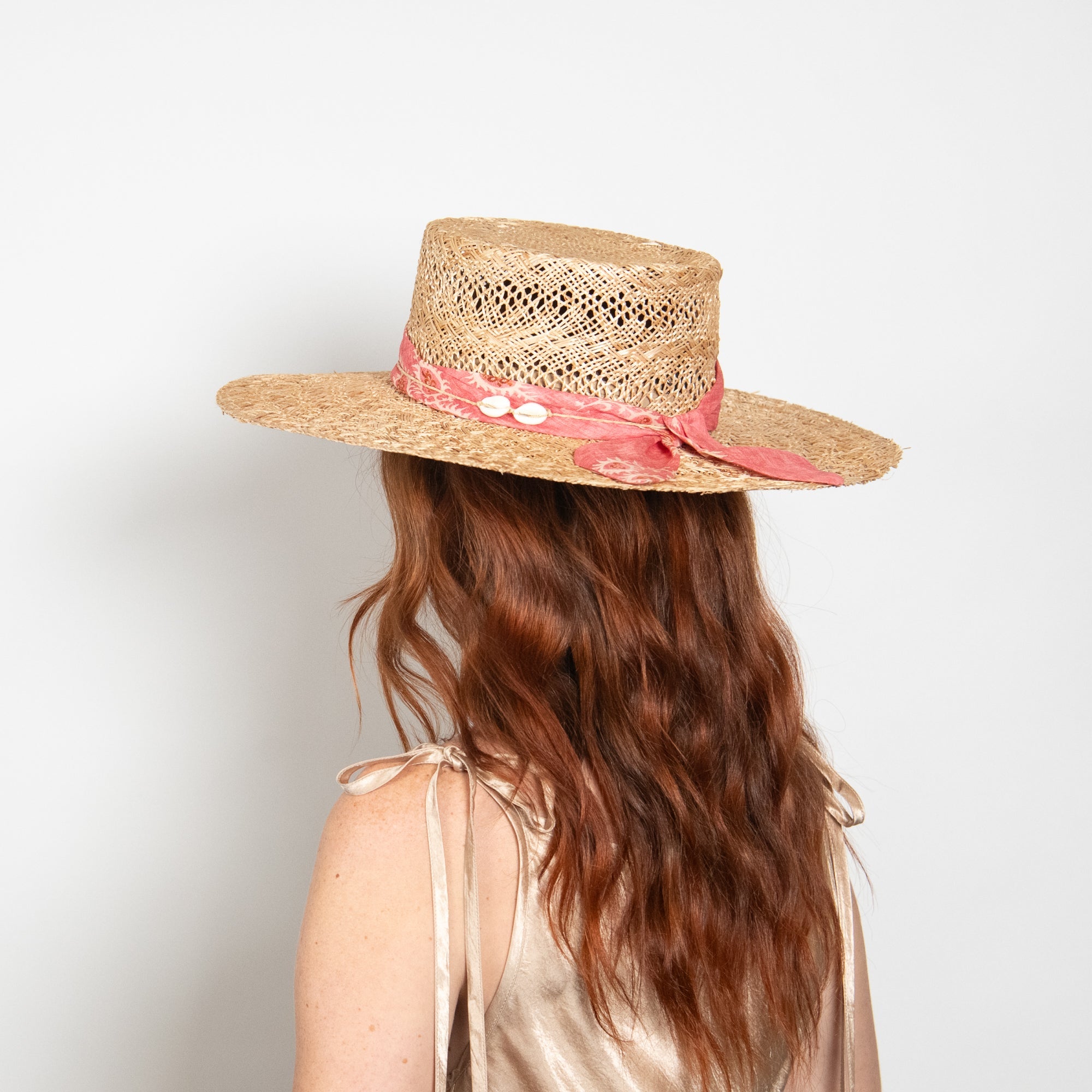 Person wearing a straw hat with a pink band on a plain background