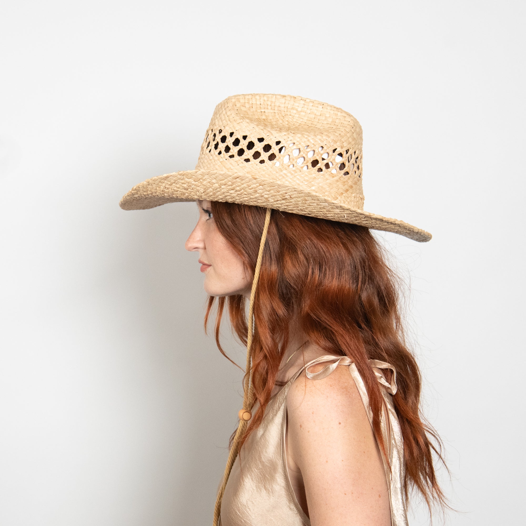 Woman wearing a straw hat with cut-out details on a light gray background