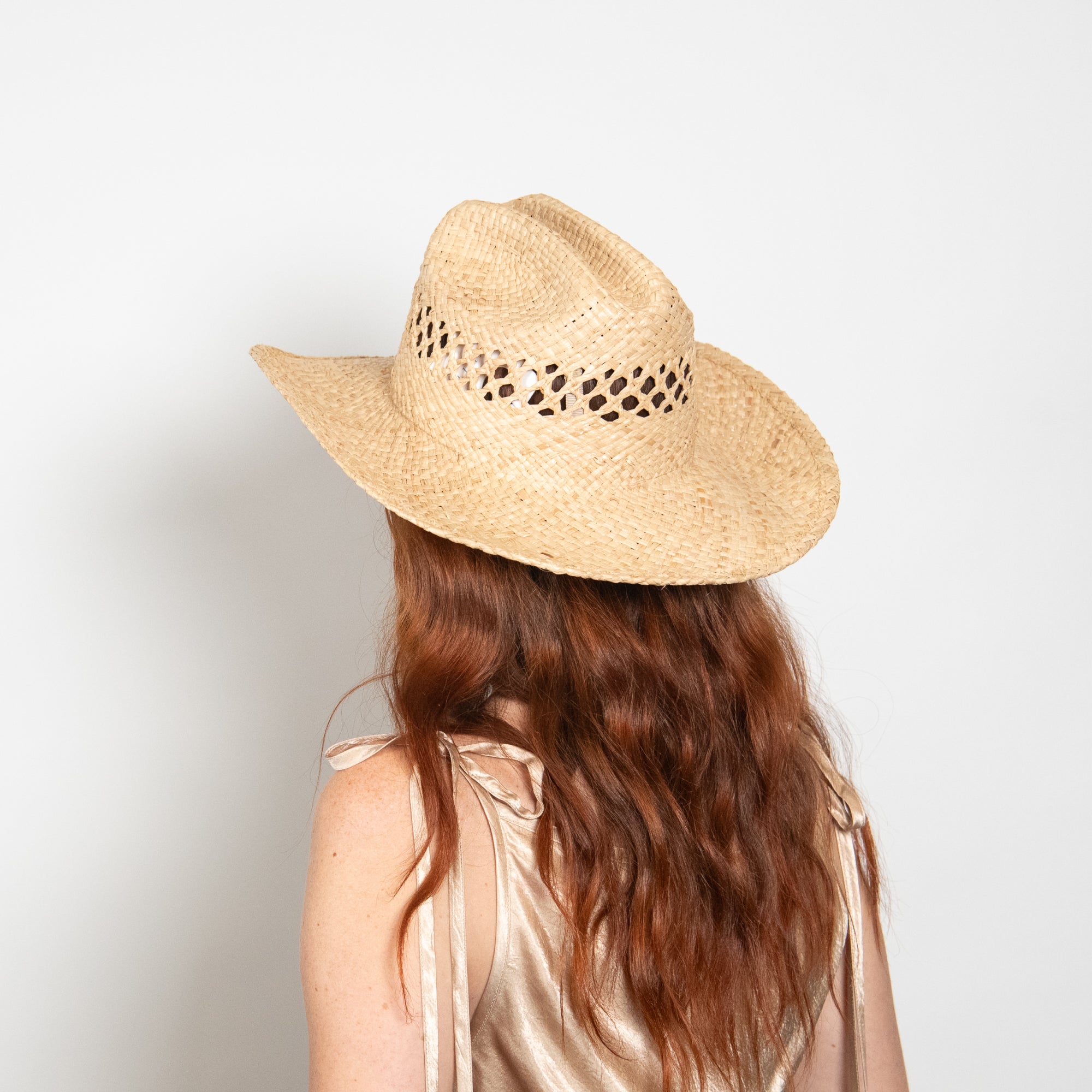 Person wearing a straw hat with cut-out details on a plain background