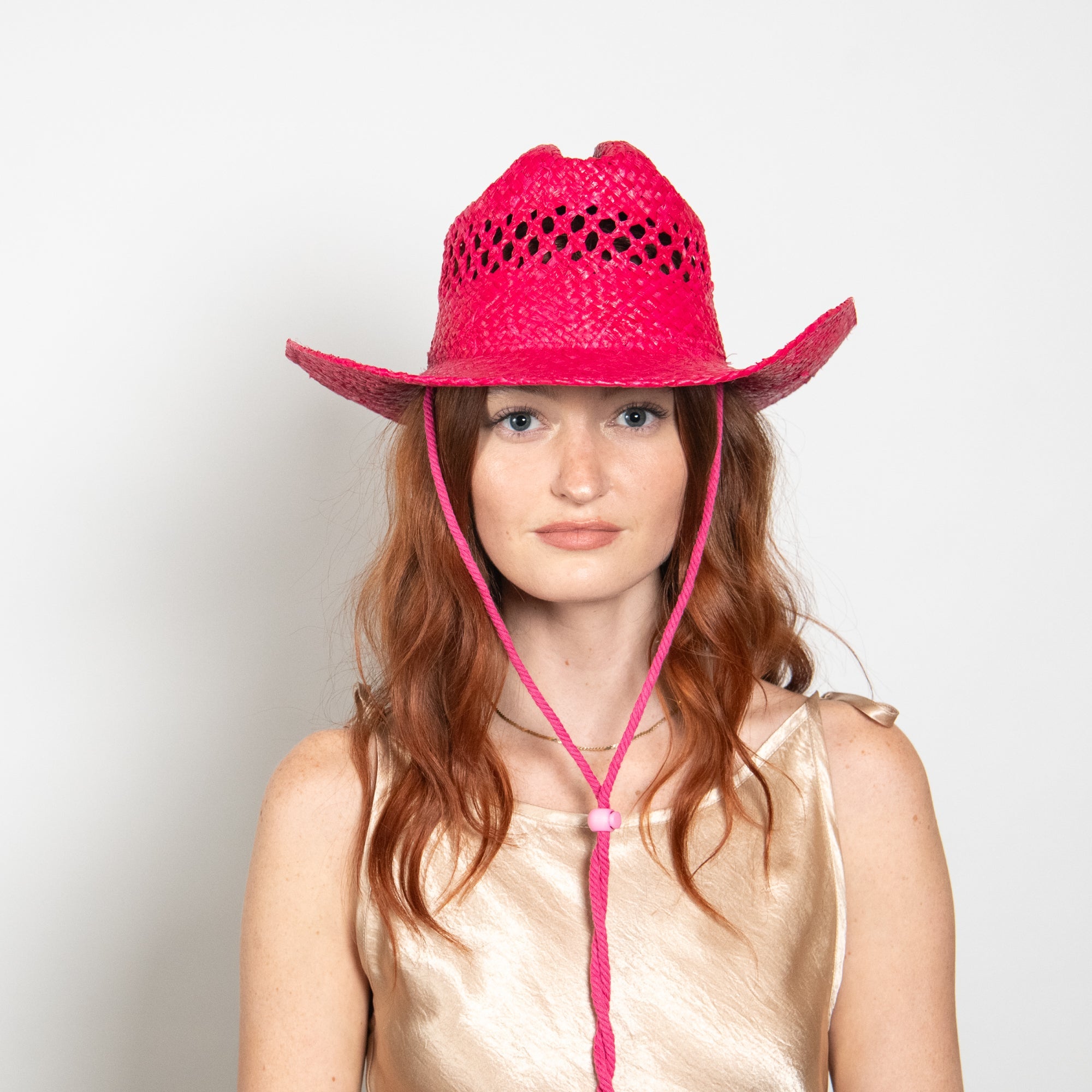 Woman wearing a pink cowboy hat with a lariat tie against a white background